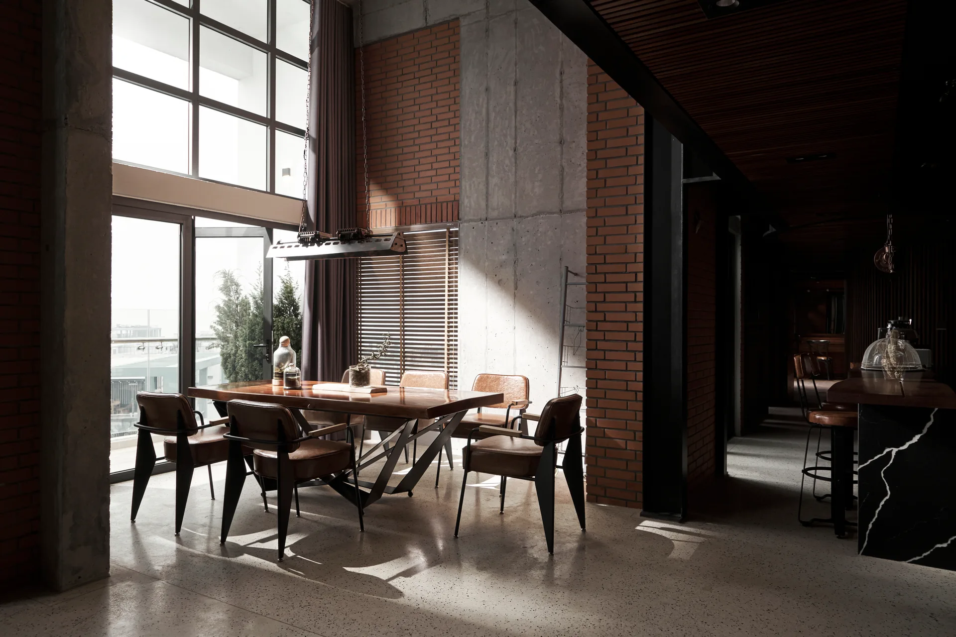 An industrial dining room featuring a wood table, leather chairs, and walls made of exposed red brick and raw concrete.