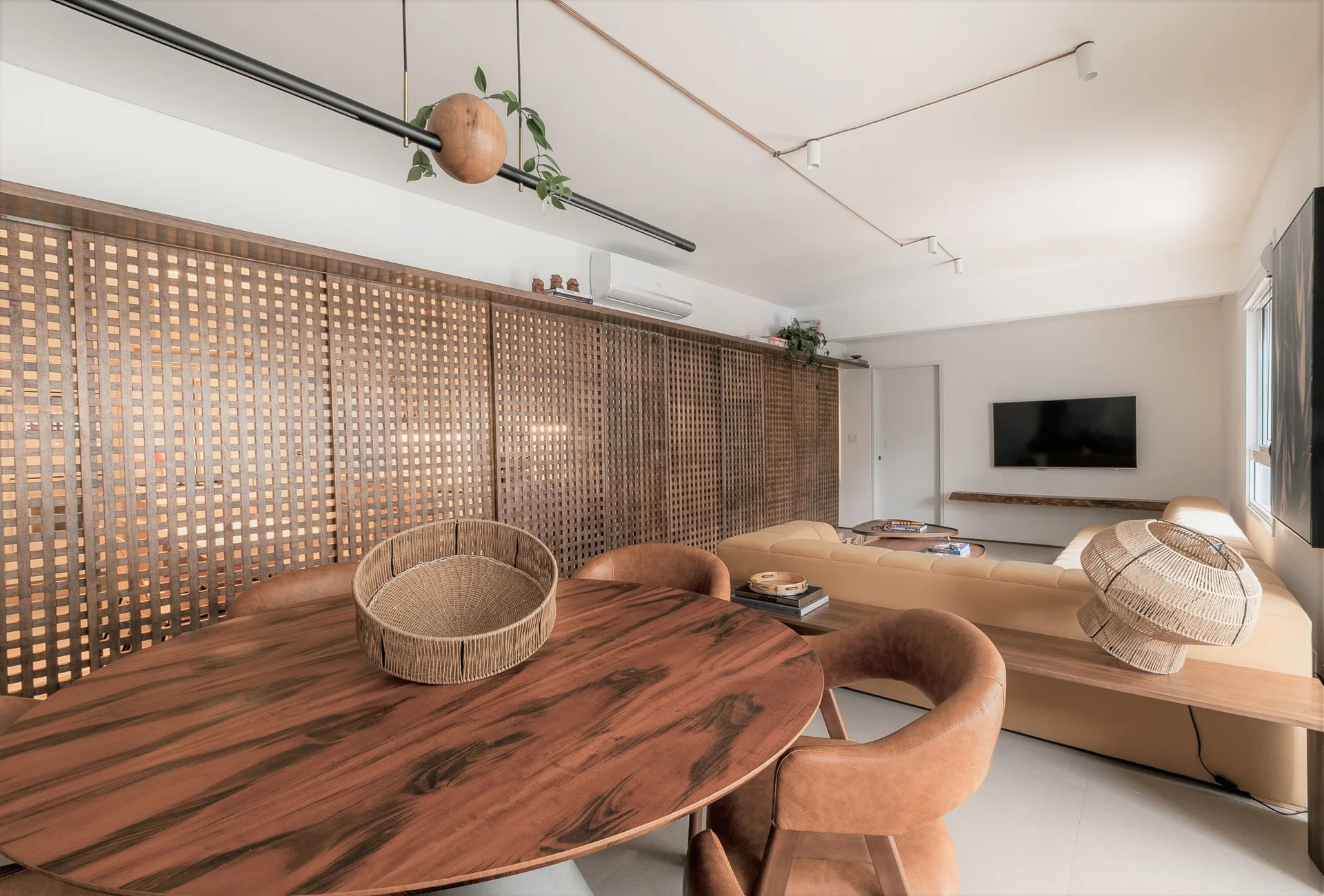 An open-plan living and dining area features a large round wooden table, tan sectional sofa, and a floor-to-ceiling wood lattice screen.