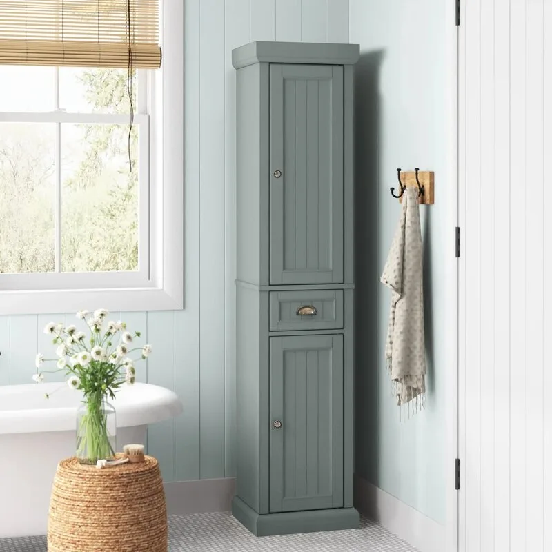 A tall blue-gray storage cabinet stands in a bathroom corner with light blue wood wall paneling next to a woven stool and bathtub.