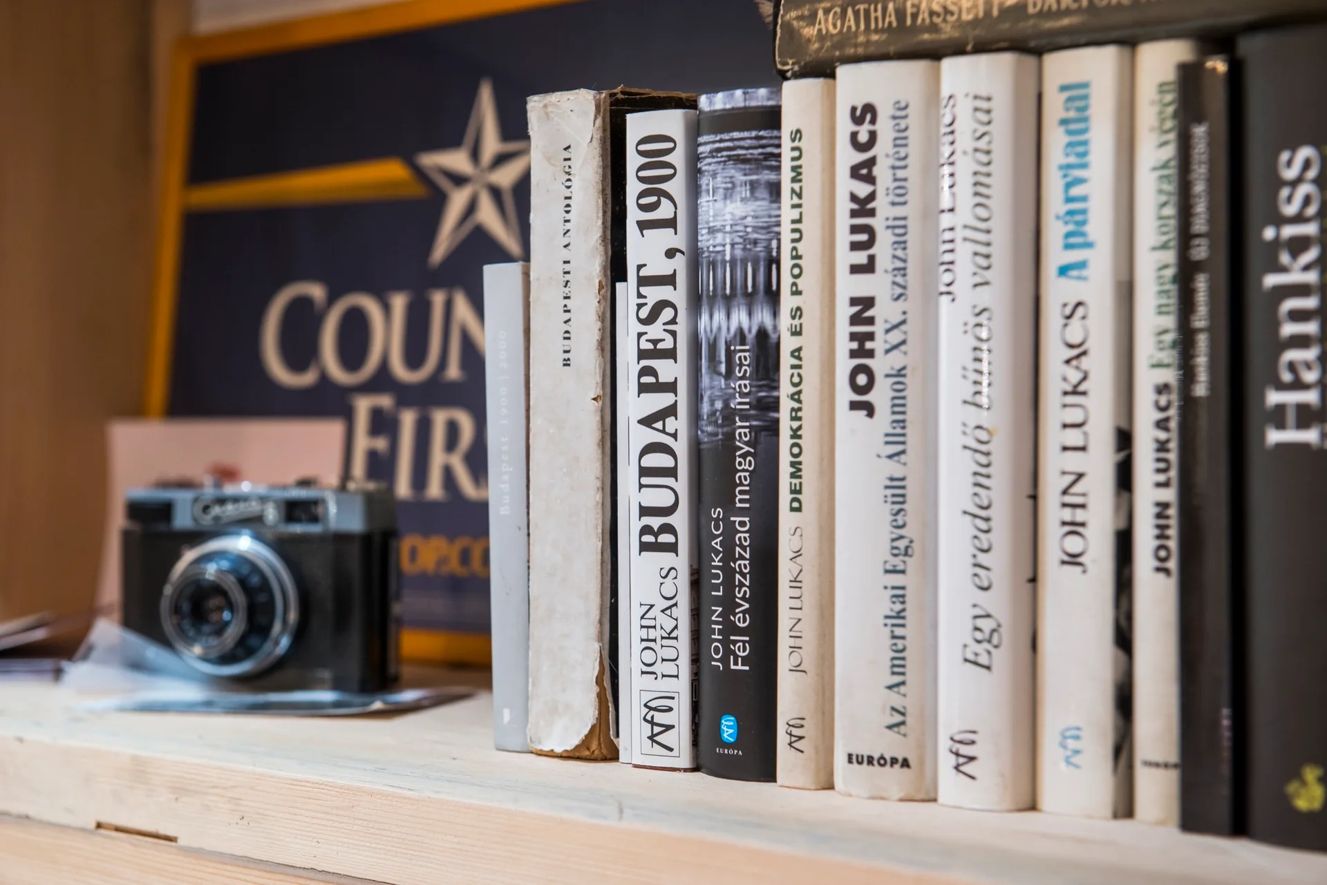 A close-up of a light wood shelf displaying a row of vintage books with black and white spines alongside an old black analog camera.