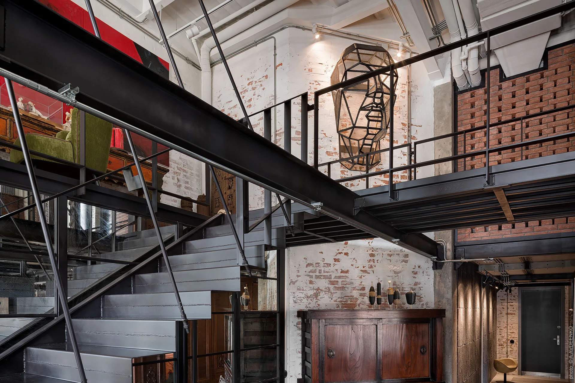 A black steel staircase and mezzanine platform in an industrial loft with a whitewashed brick wall and wire mesh sculpture.