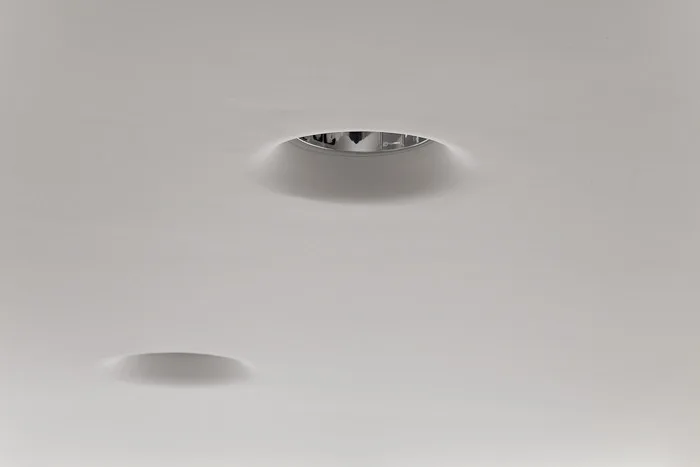 Two circular recessed ceiling lights blend seamlessly into a smooth matte white plaster surface.
