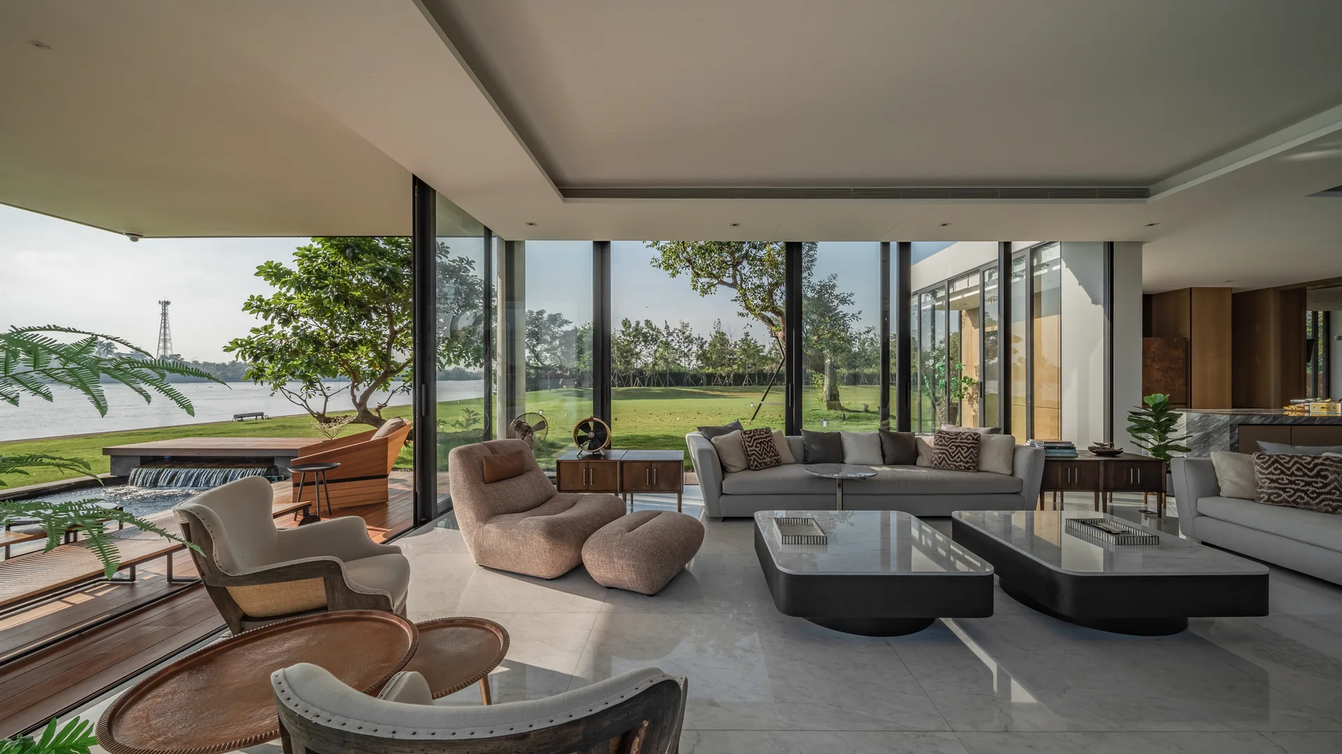 A spacious modern living room features polished marble floors, contemporary sofas, and floor-to-ceiling sliding glass doors opening to a grassy lawn.