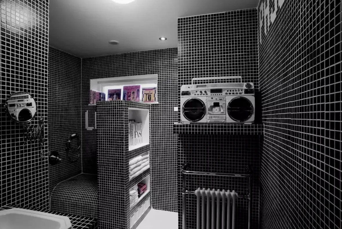 A bathroom clad in small black grid tiles with white grout, featuring a built-in towel niche, a vintage white boombox, and a chrome towel radiator.