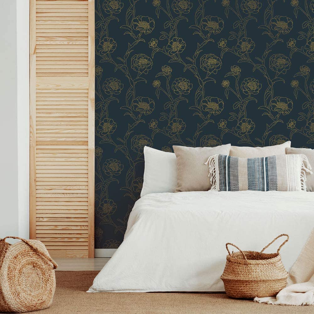 A bed with white bedding stands against a dark navy wallpaper with gold floral patterns, next to a louvered wooden folding screen.