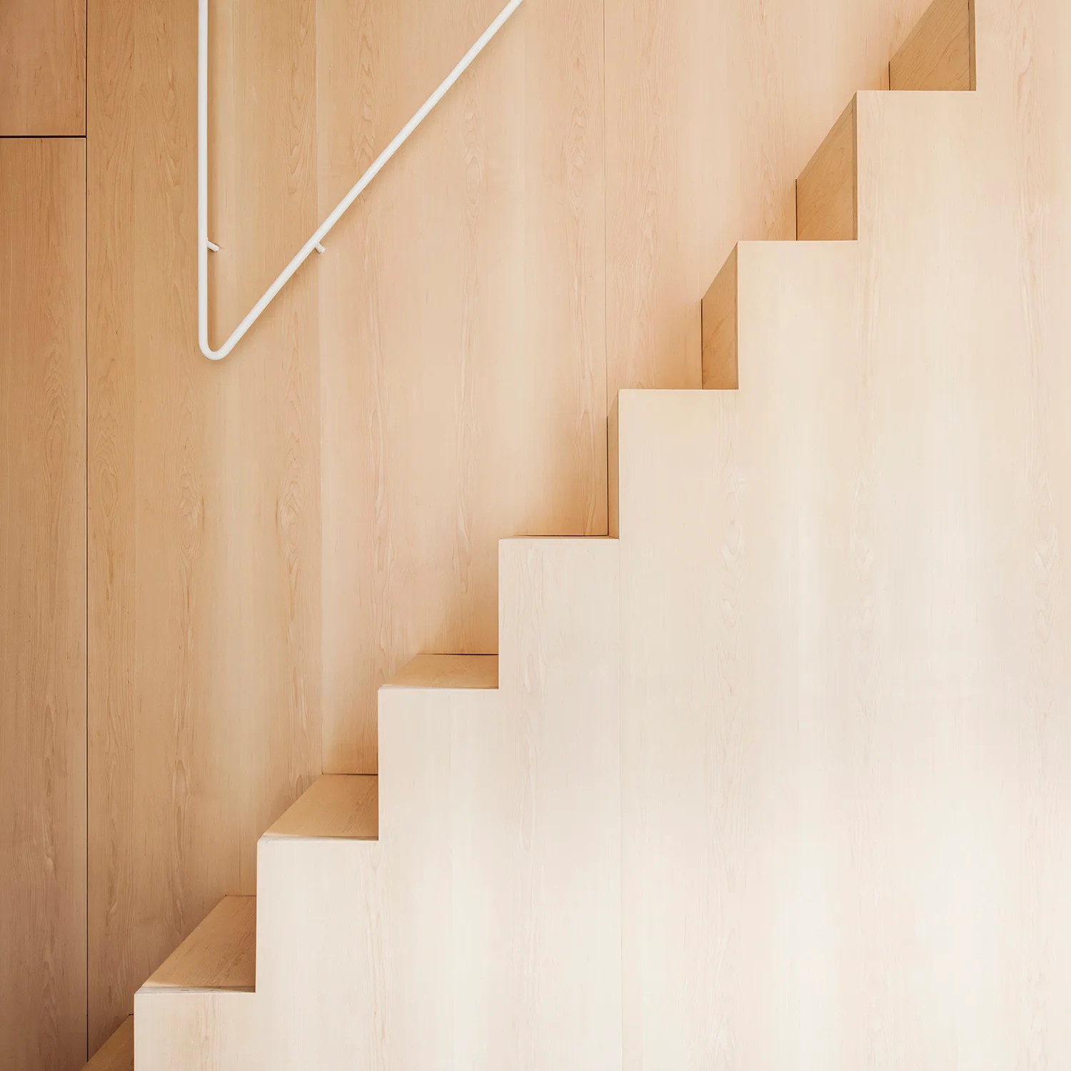 A minimalist staircase crafted from light wood is integrated against matching vertical wood paneling and paired with a slim white handrail.