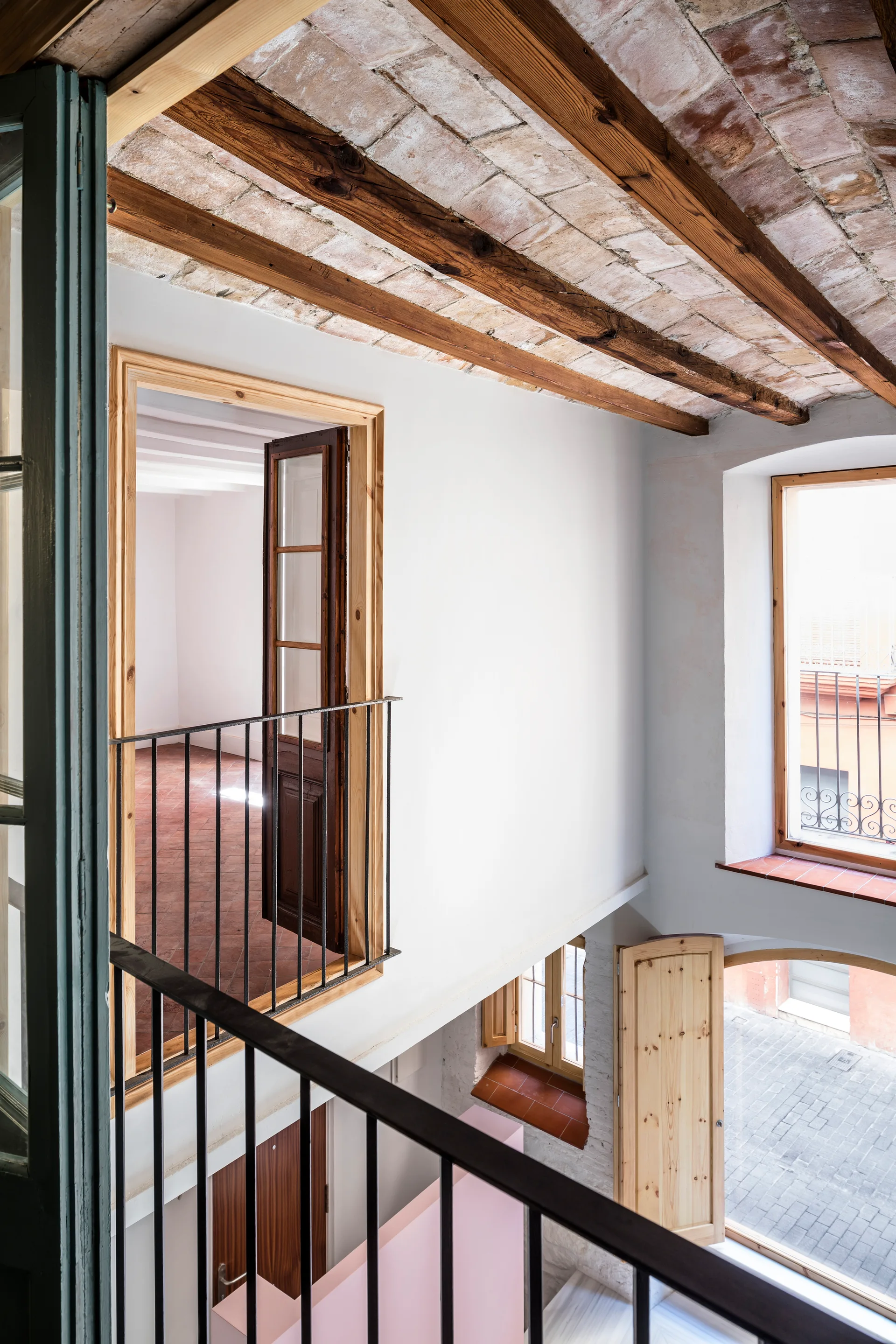 A multi-level interior stairwell featuring an exposed brick vaulted ceiling with wood beams, white walls, and black metal railings.