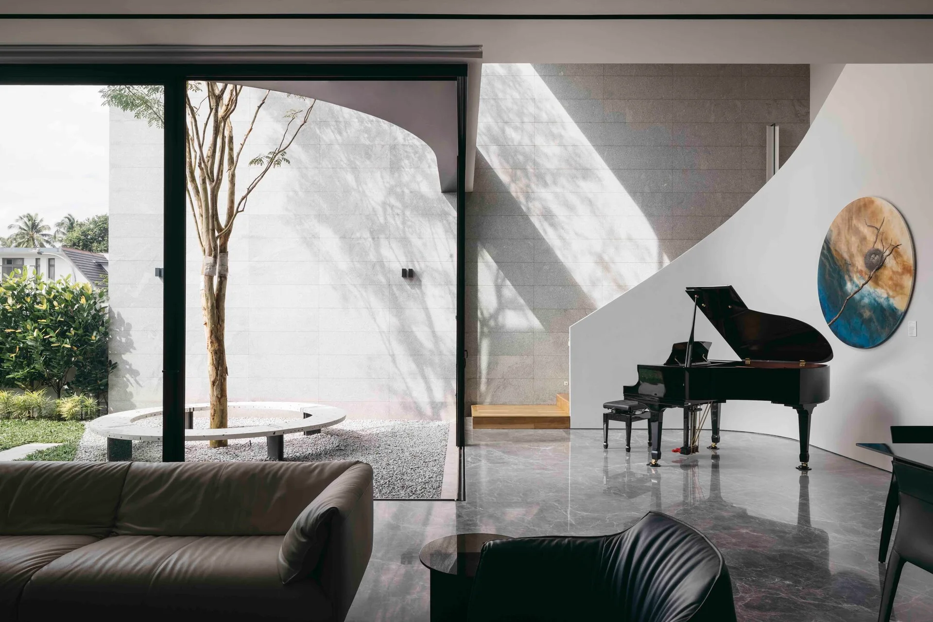 A minimalist living room with a black grand piano, polished marble floors, and large glass doors opening to a courtyard with a tree.