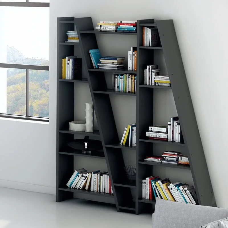A dark charcoal gray geometric bookshelf with diagonal frame supports stands against a white wall, styled with books and a white ceramic vase.