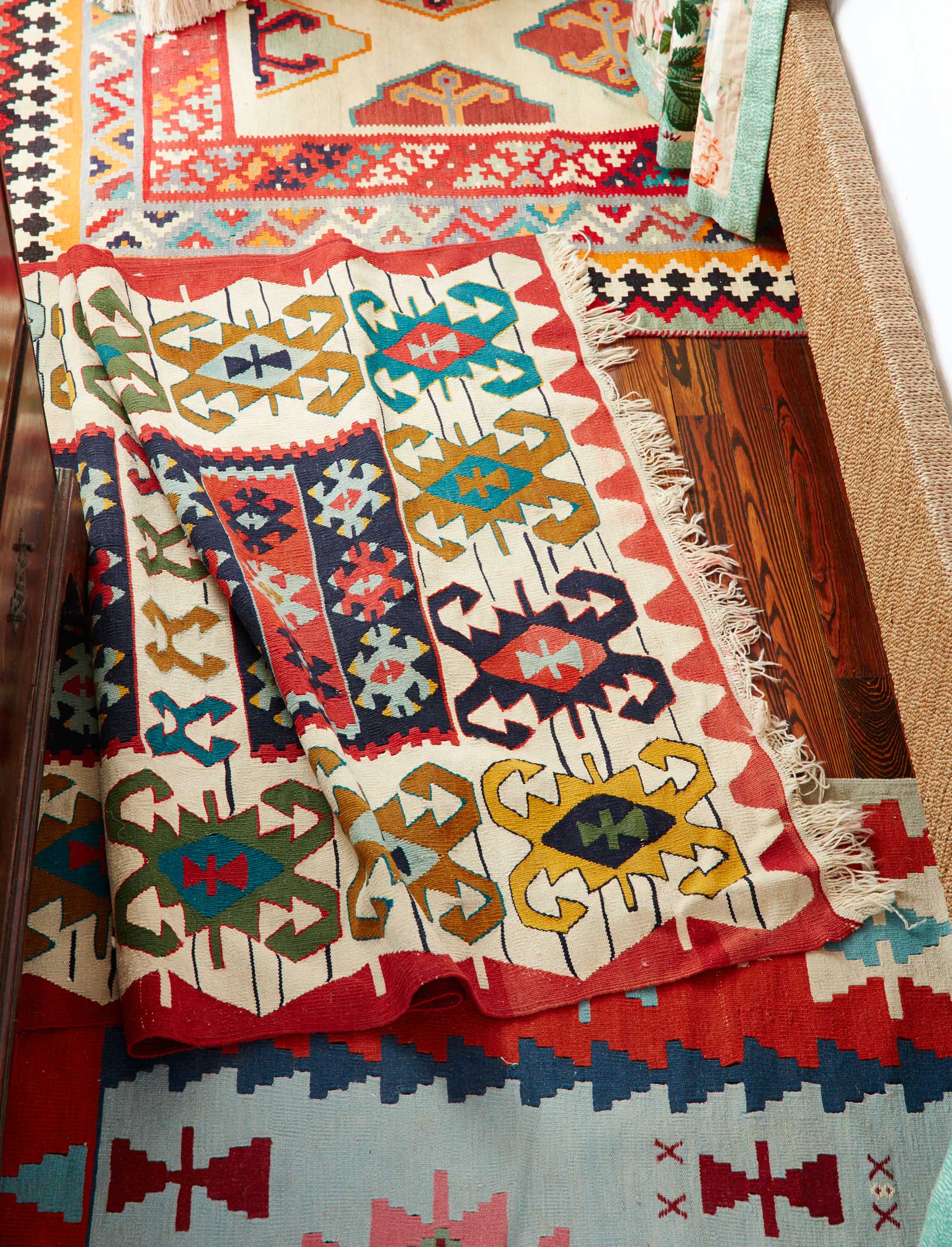 Multiple colorful kilim rugs with geometric patterns and fringe are layered over a dark hardwood floor.