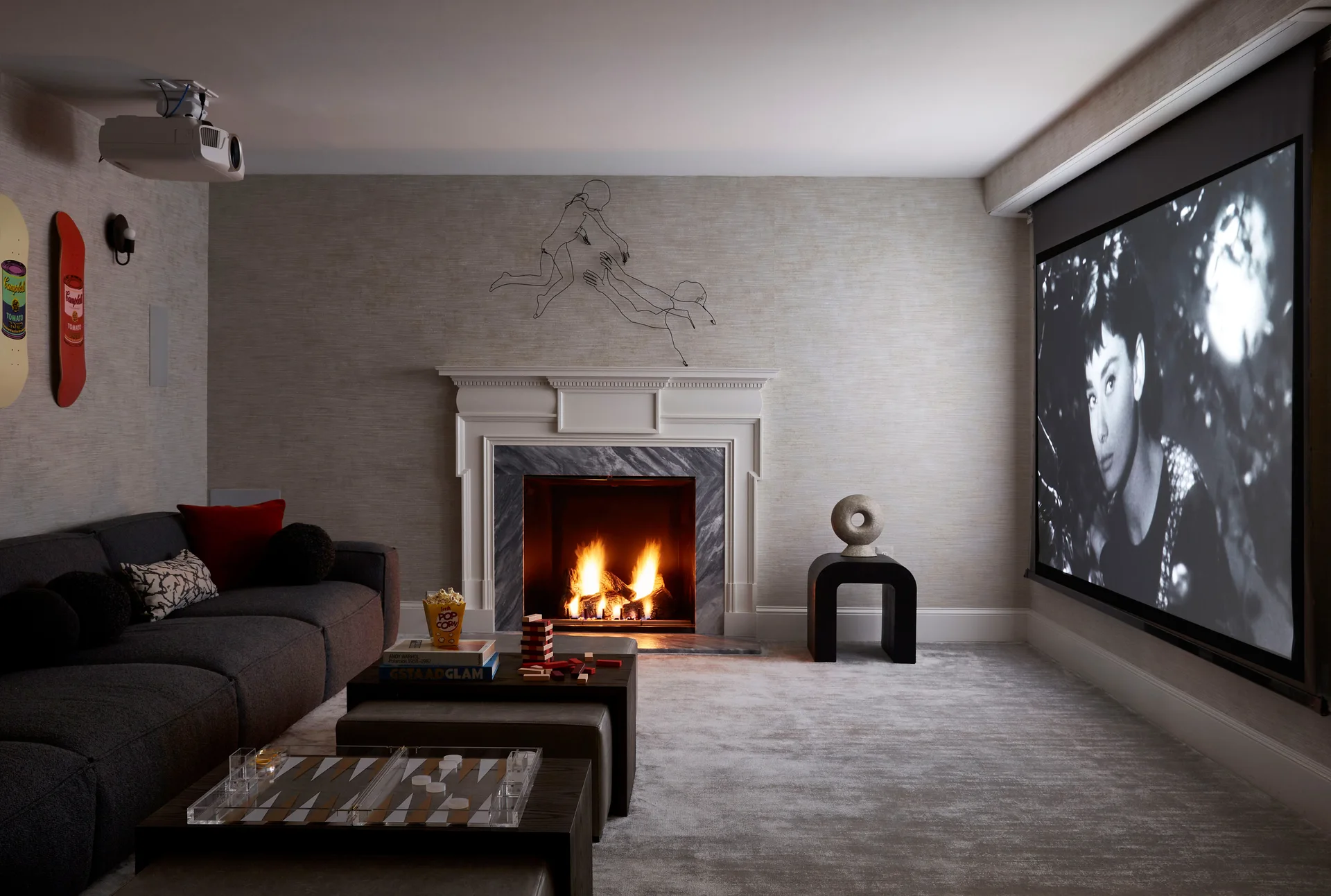 A cozy media room features a grey sectional sofa facing a white-mantel fireplace next to a large projector screen on an adjacent wall.