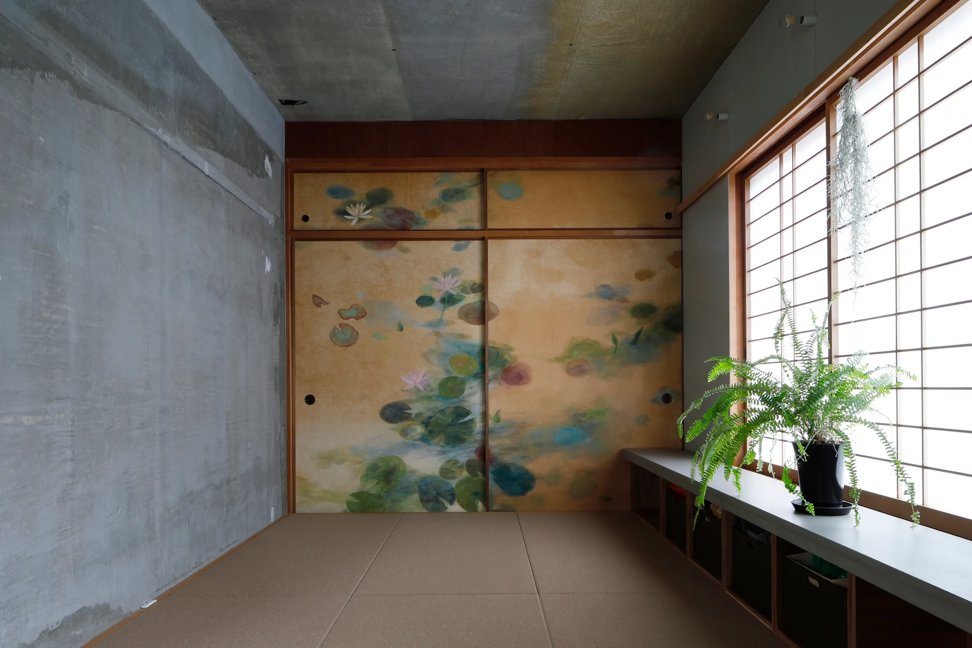 A Japanese-style room features concrete walls, tatami floor mats, a shoji window, and sliding doors painted with water lilies.