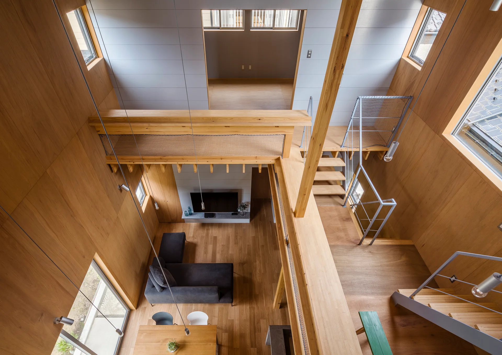 High-angle view of a modern living room featuring warm wood-paneled walls, an elevated wooden loft, a dark gray sectional sofa, and a staircase.