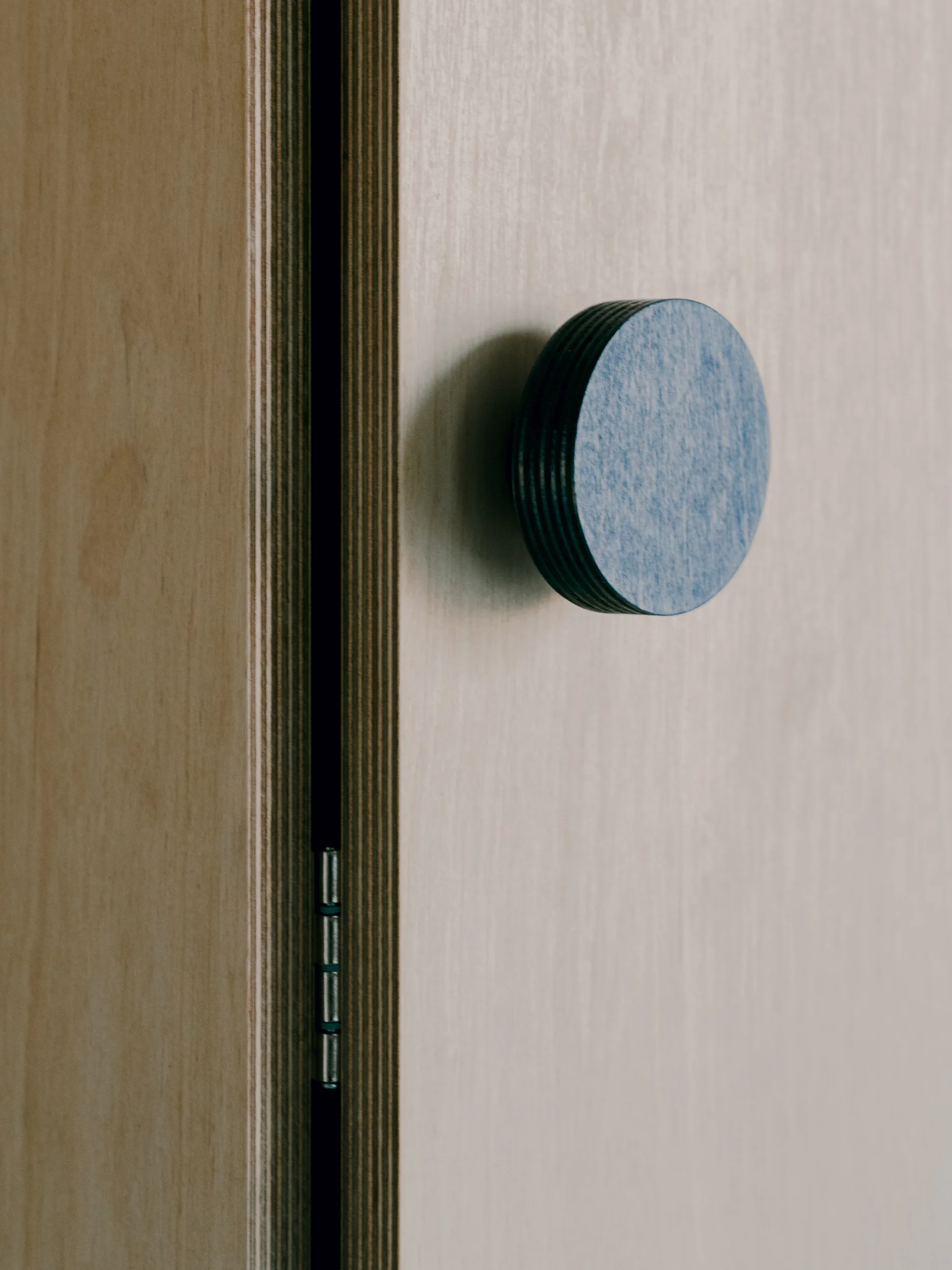 Close-up of a light plywood cabinet door showing the exposed layered edge and a round matte blue wooden knob.
