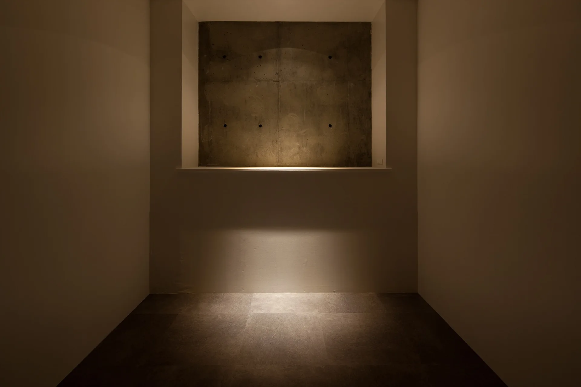 A minimalist recessed square wall alcove features a raw concrete panel accented by warm, downward-facing integrated lighting.
