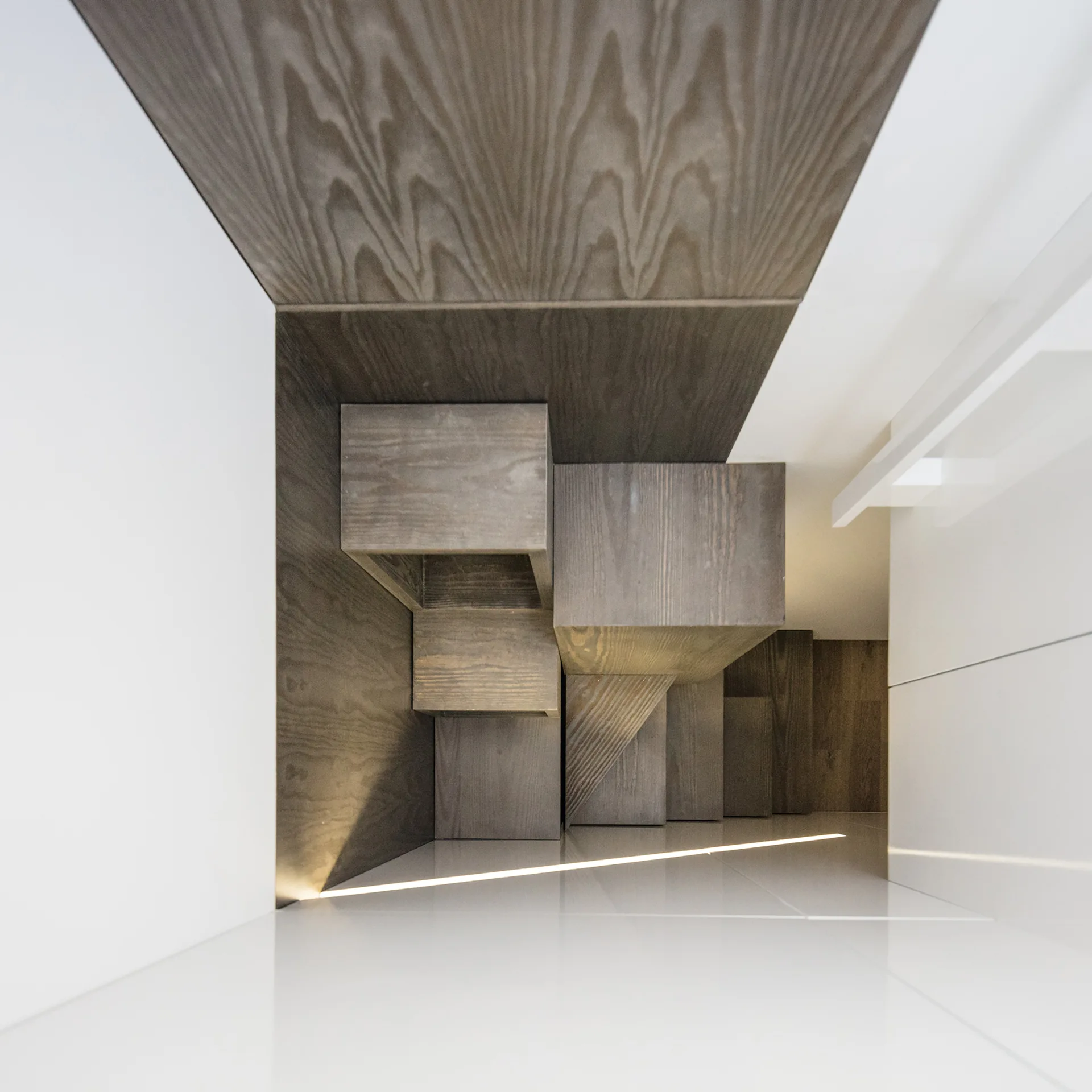 A high-angle view looking down a modern staircase with dark wood-grain steps framed by glossy white walls and a glowing linear light strip.