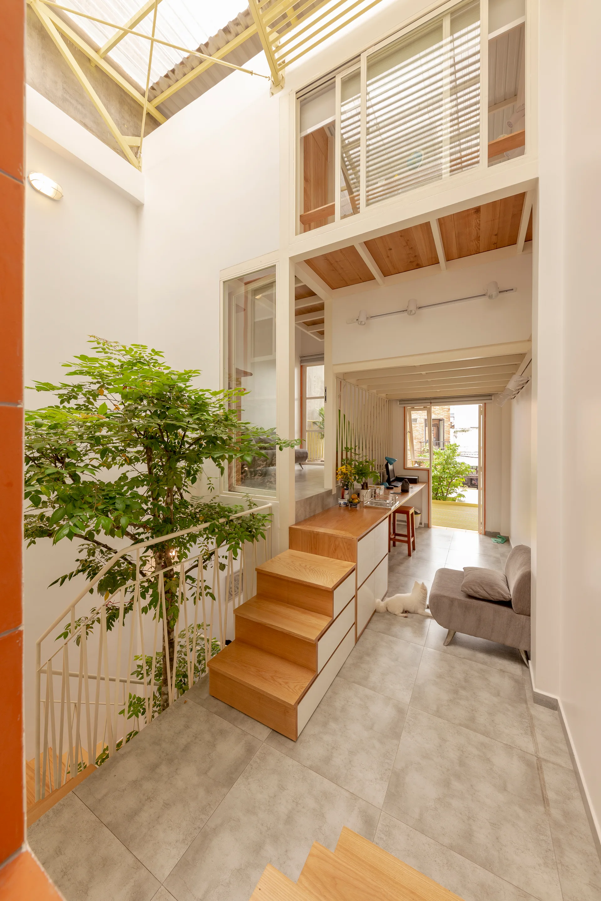 A multi-level home interior featuring wood stairs, an integrated indoor tree, built-in storage drawers, and gray tile flooring.