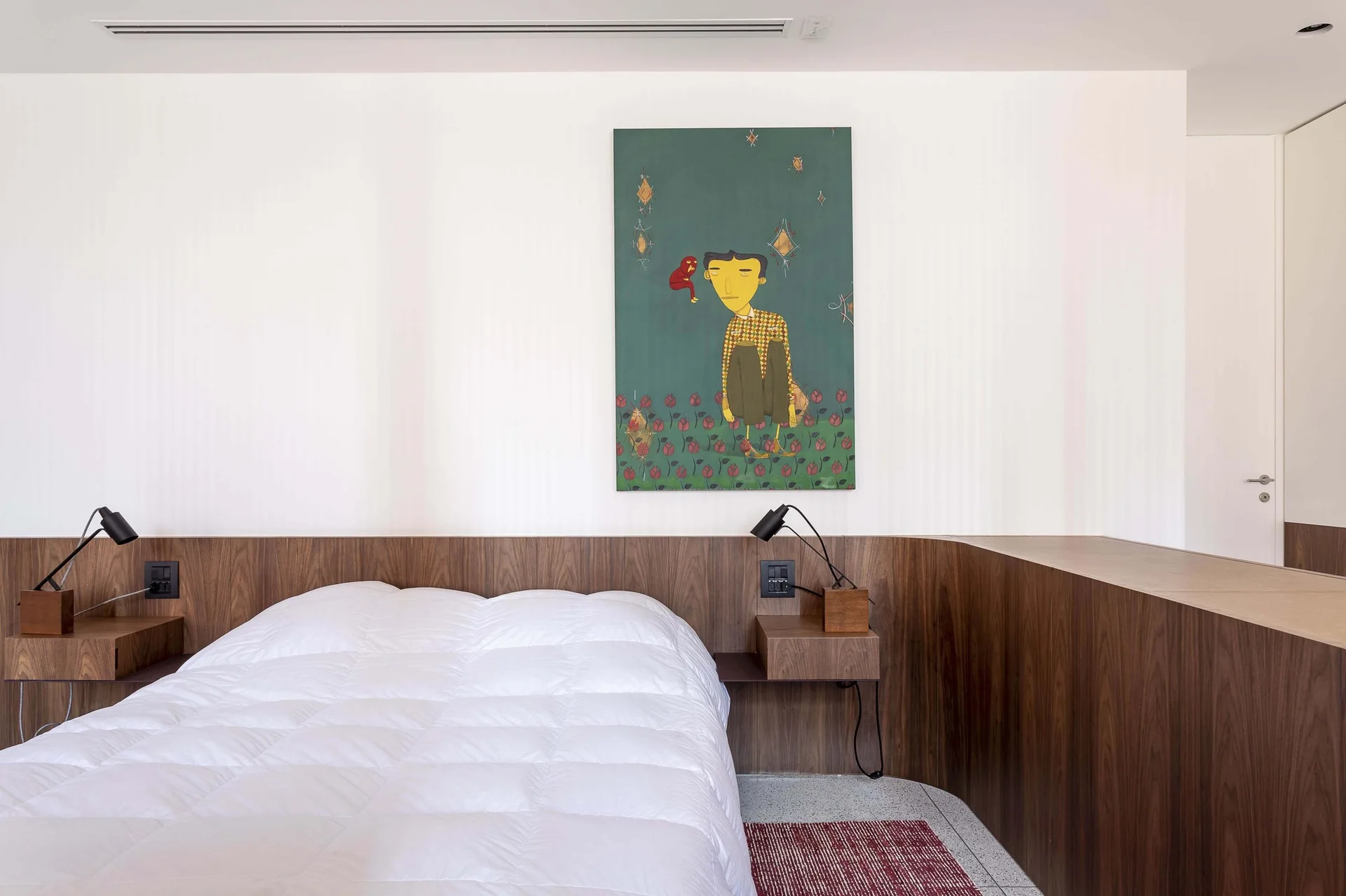 A minimalist bedroom featuring a white bed set against a continuous wood-paneled wall with integrated nightstands and a green portrait painting.