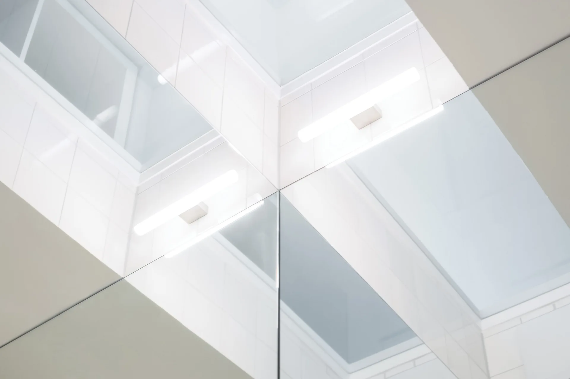 A close-up view of a clean corner featuring white grid wall tiles, a reflective mirror, and integrated linear light fixtures.