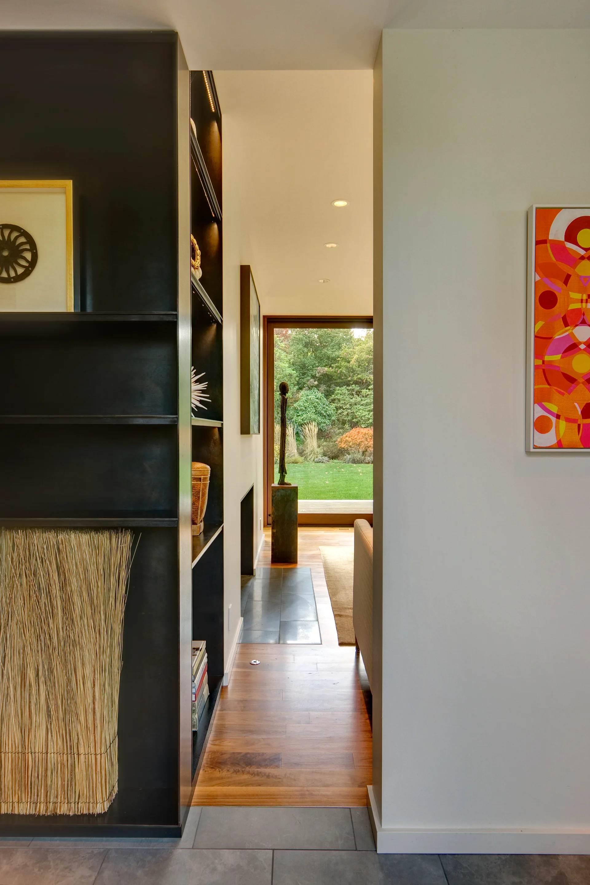 A bright hallway featuring custom black shelving, warm wood flooring, and a glass door opening to a green garden.