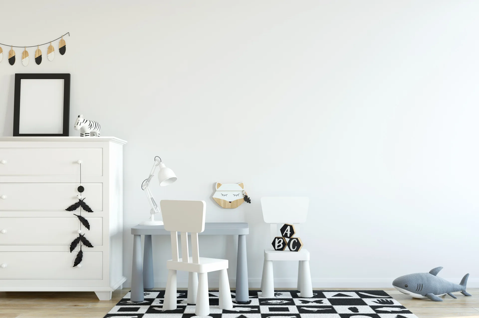 A children's play area features a white dresser, a grey play desk with white chairs, and a black and white patterned rug against a plain white wall.