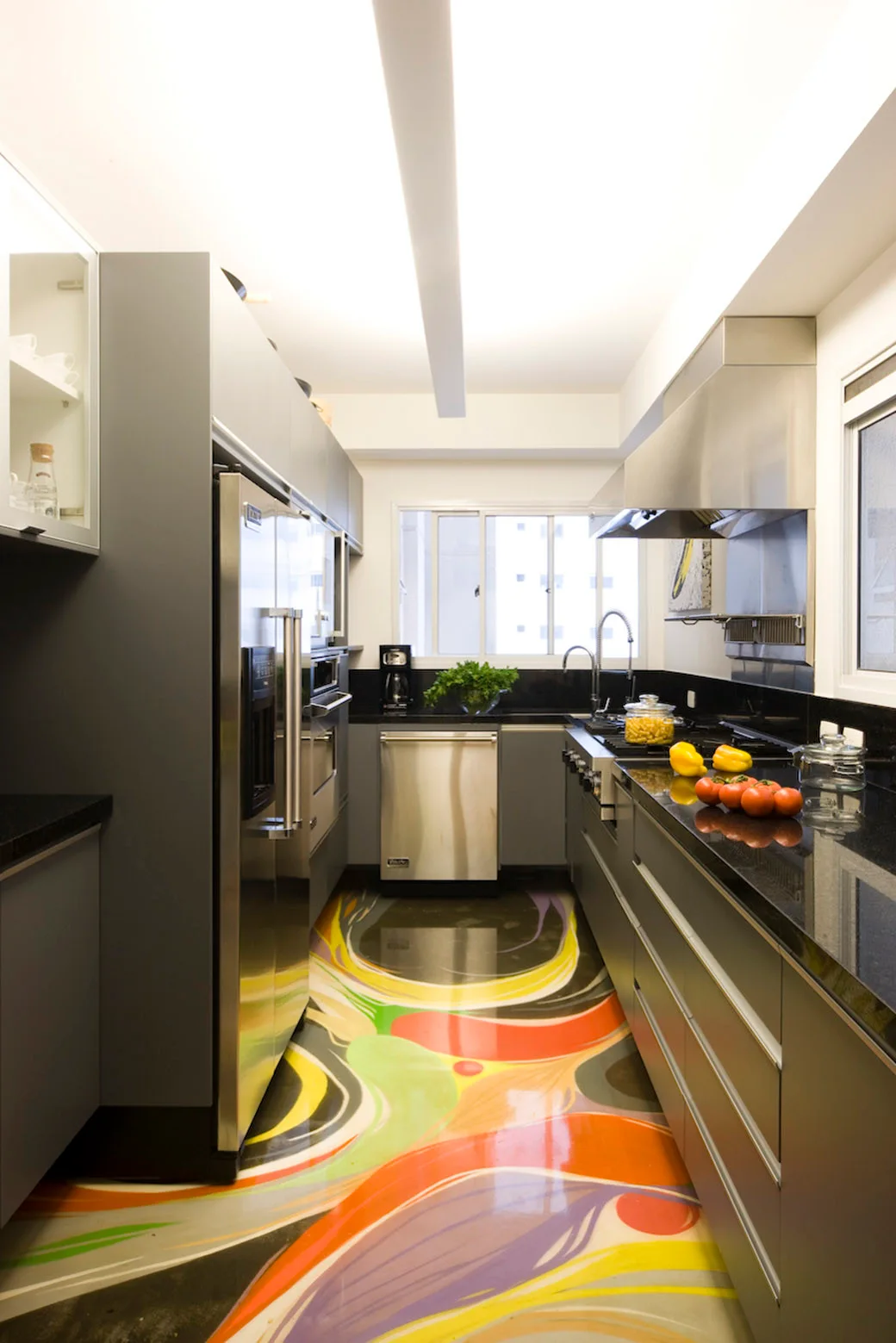 A galley kitchen featuring matte grey cabinets, stainless steel appliances, black stone countertops, and a glossy, multi-colored abstract painted floor.