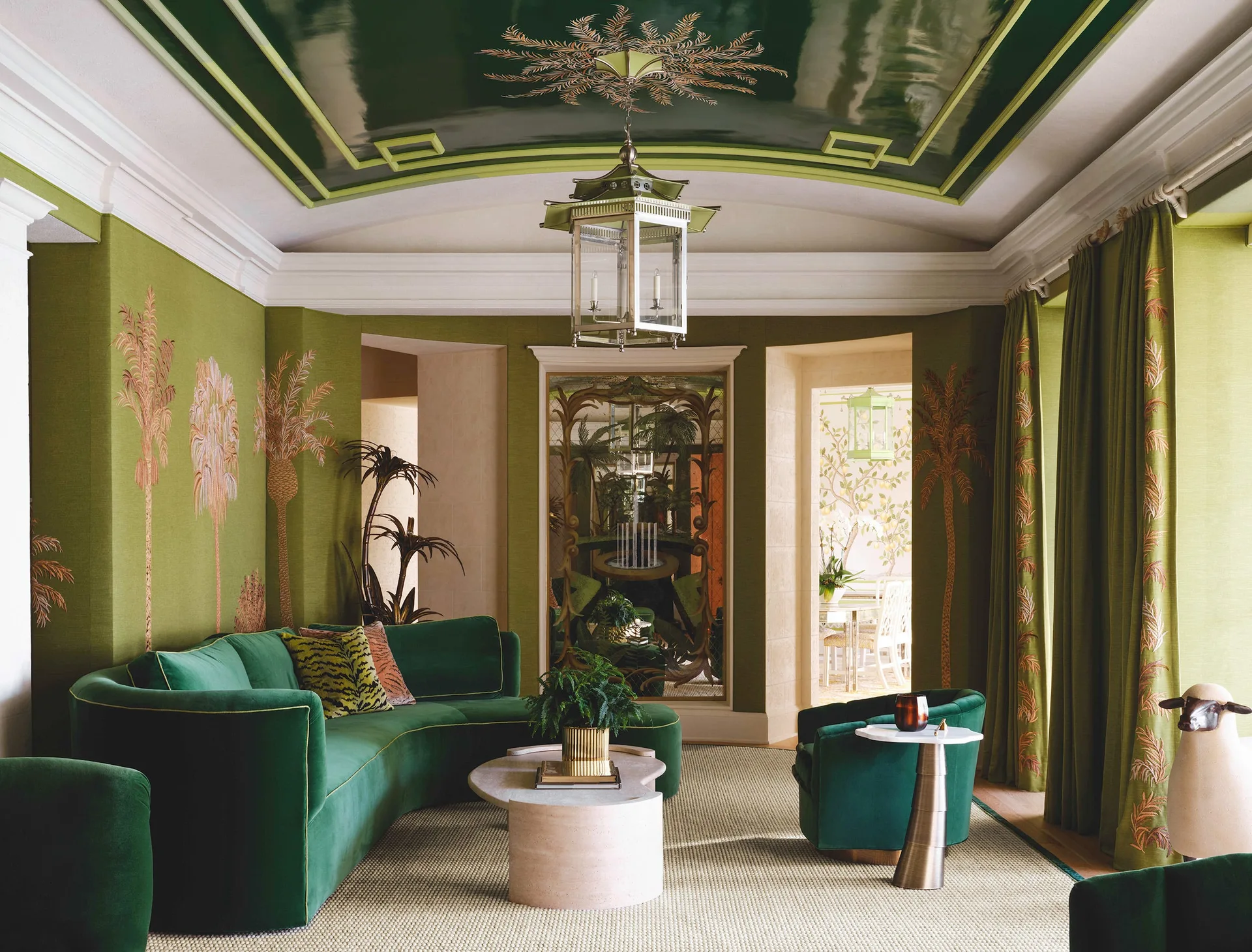 A green living room features a curved velvet sofa, palm-patterned wallpaper, and a reflective, high-gloss lacquered tray ceiling with a hanging lantern.