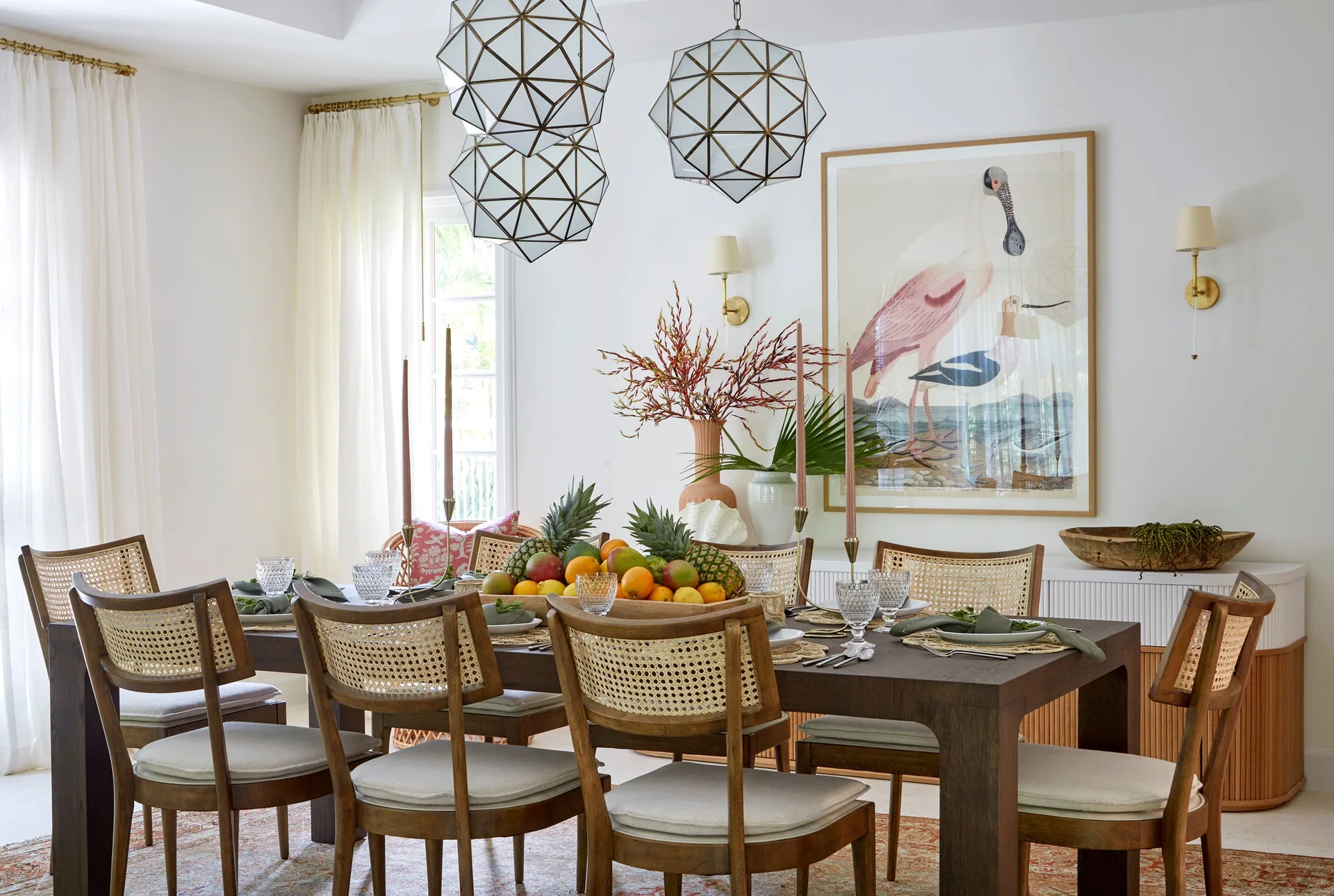A dining room features a dark wood table with cane-back chairs, geometric pendant lights, and a large bird art print on the wall.