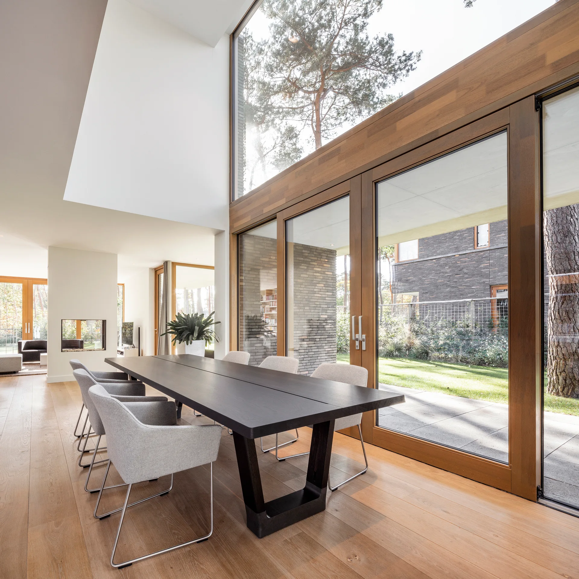 A dark wood dining table and light grey chairs sit next to large wood-framed glass sliding doors looking out to a garden.