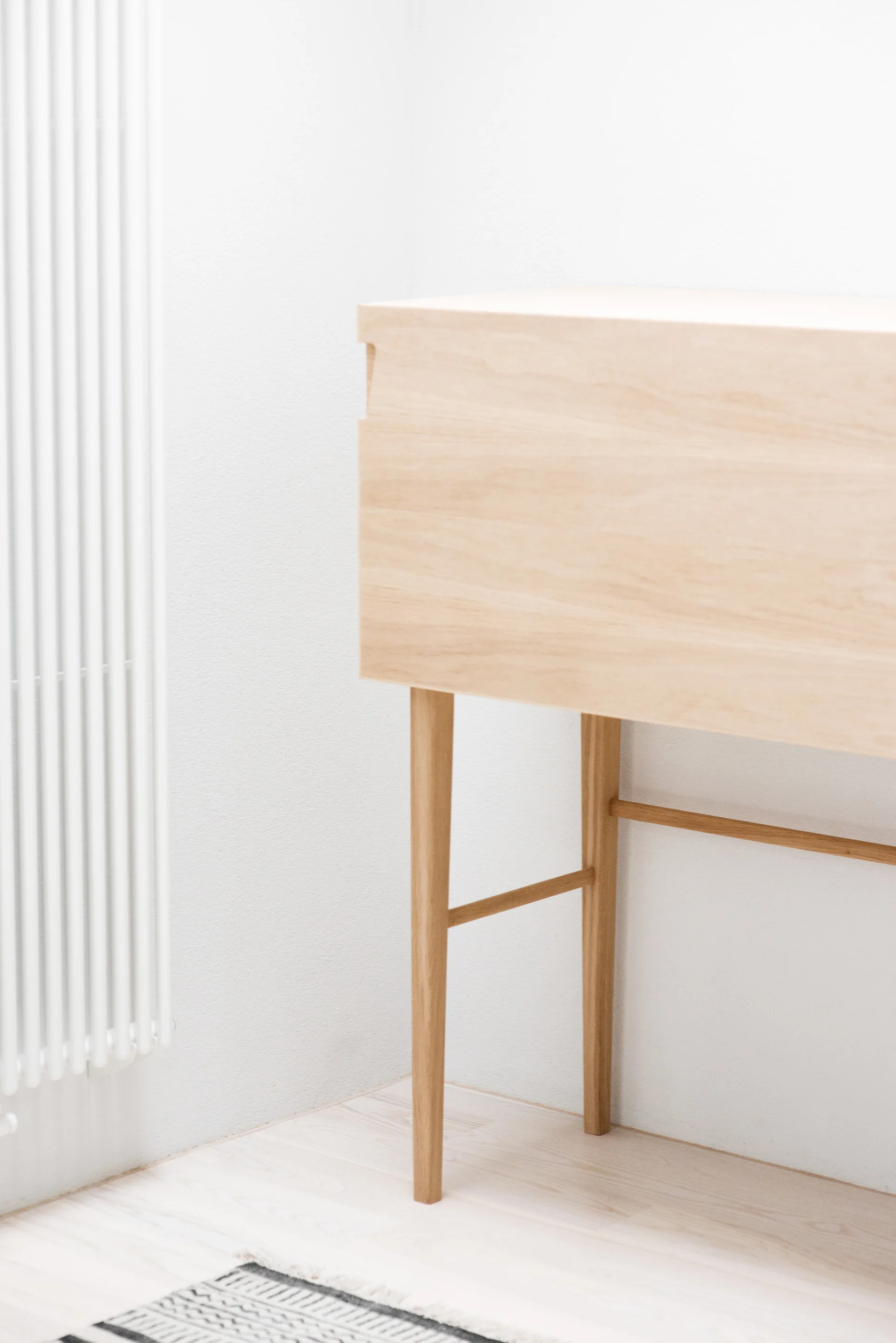 A light wood console table stands on a pale wooden floor next to a white vertical wall-mounted radiator.
