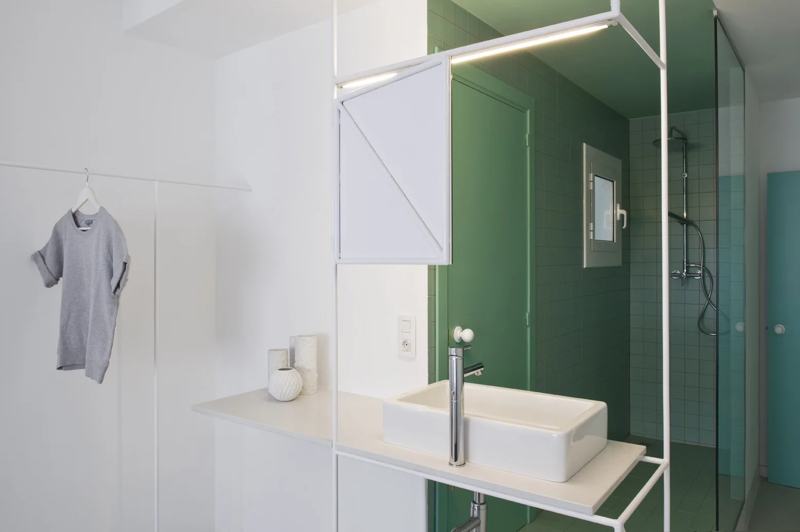 A minimalist bathroom with a white vanity sink mounted on a slim metal structure next to a green tiled shower enclosure.