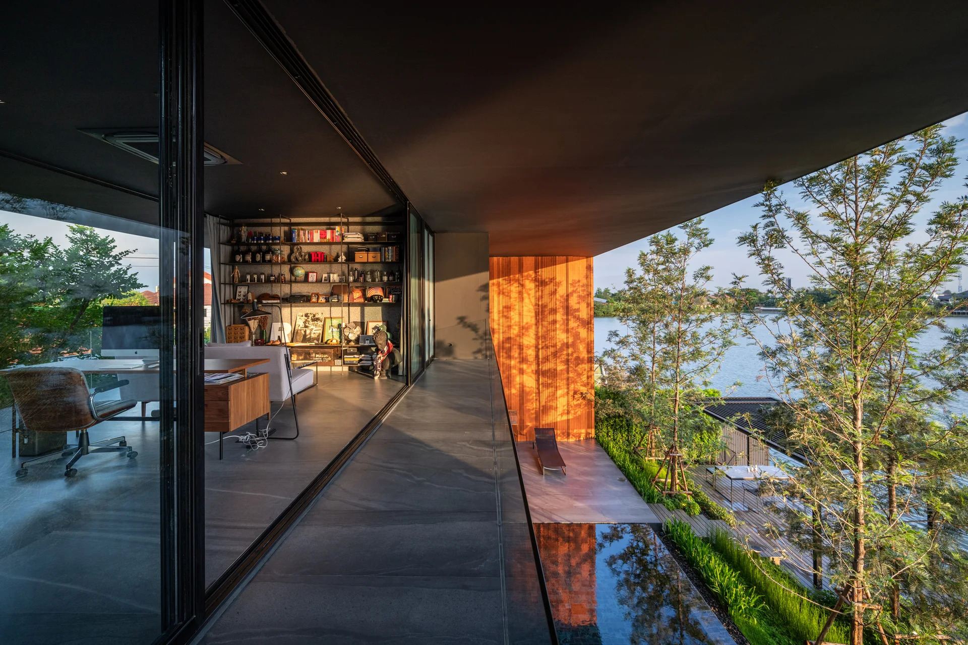 A dark charcoal home office with sliding glass doors opening to a concrete terrace with a reflection pool and wood wall.