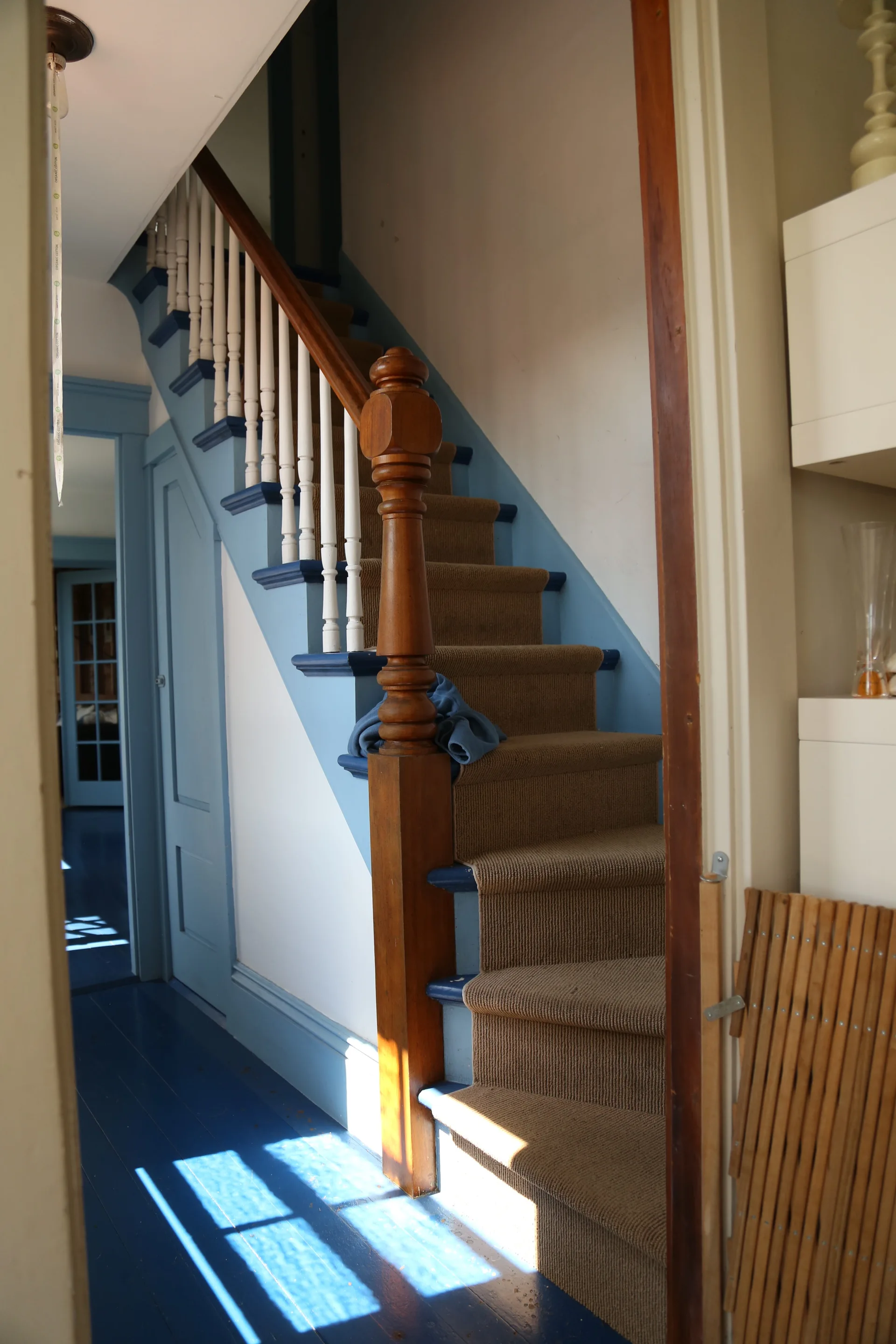 A wooden staircase features blue painted trim and risers, white balusters, a natural wood handrail, and a brown carpet runner.
