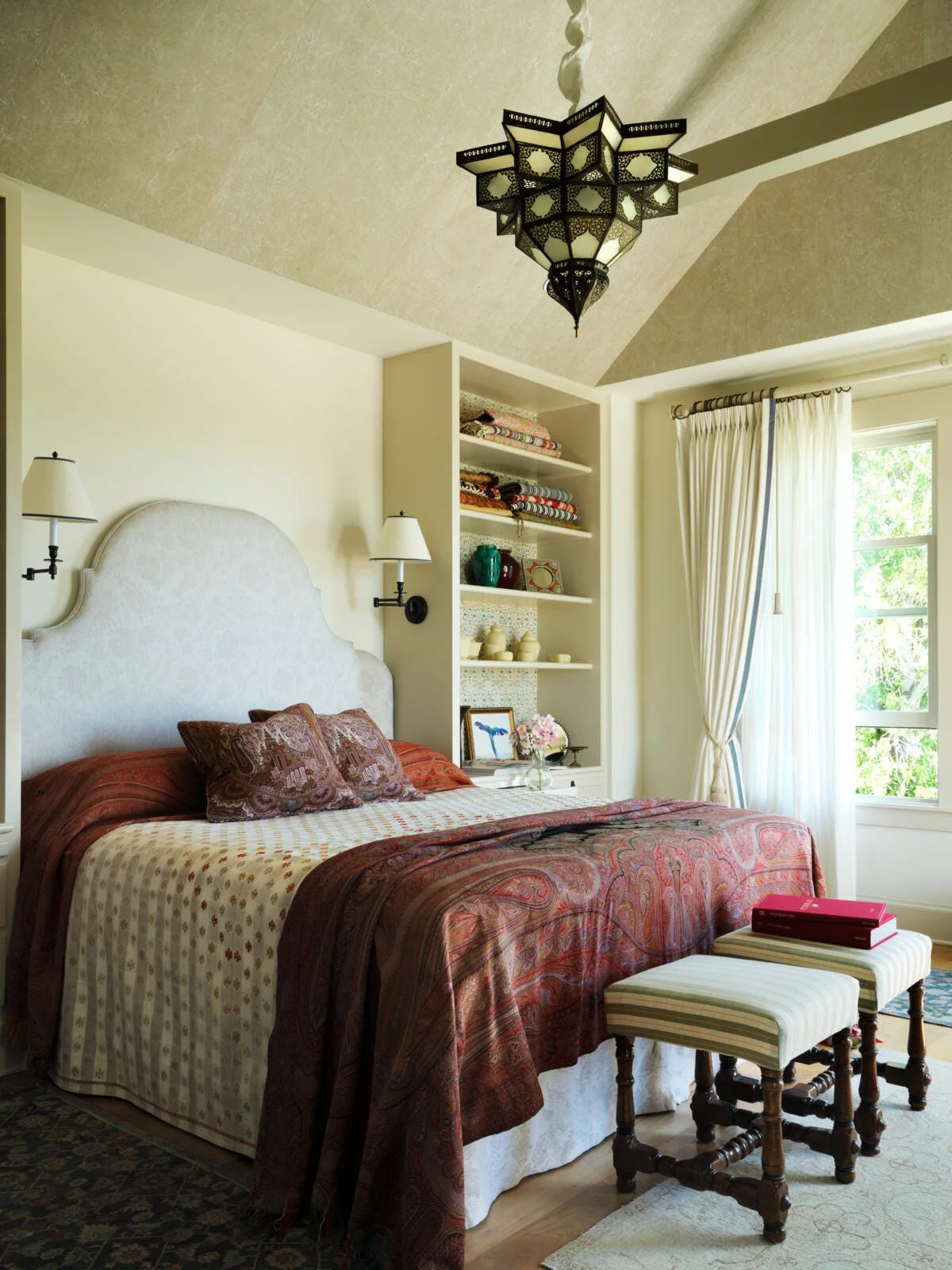 A bedroom featuring an arched headboard, terracotta paisley bedding, built-in shelving, and an ornate metal star lantern hanging from a vaulted ceiling.