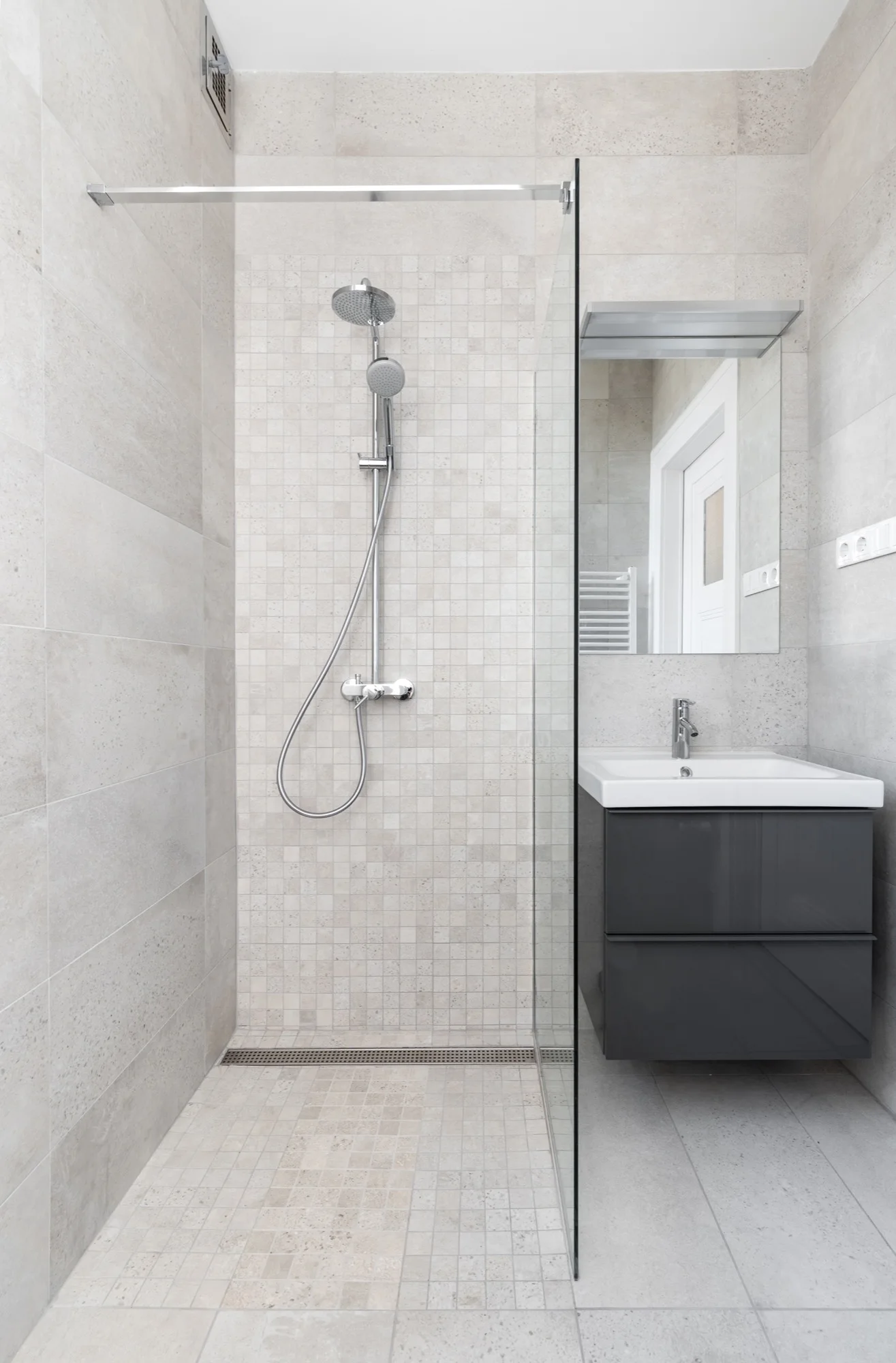 A modern bathroom featuring a walk-in shower with beige mosaic tile, a glass partition, and a dark grey floating vanity.