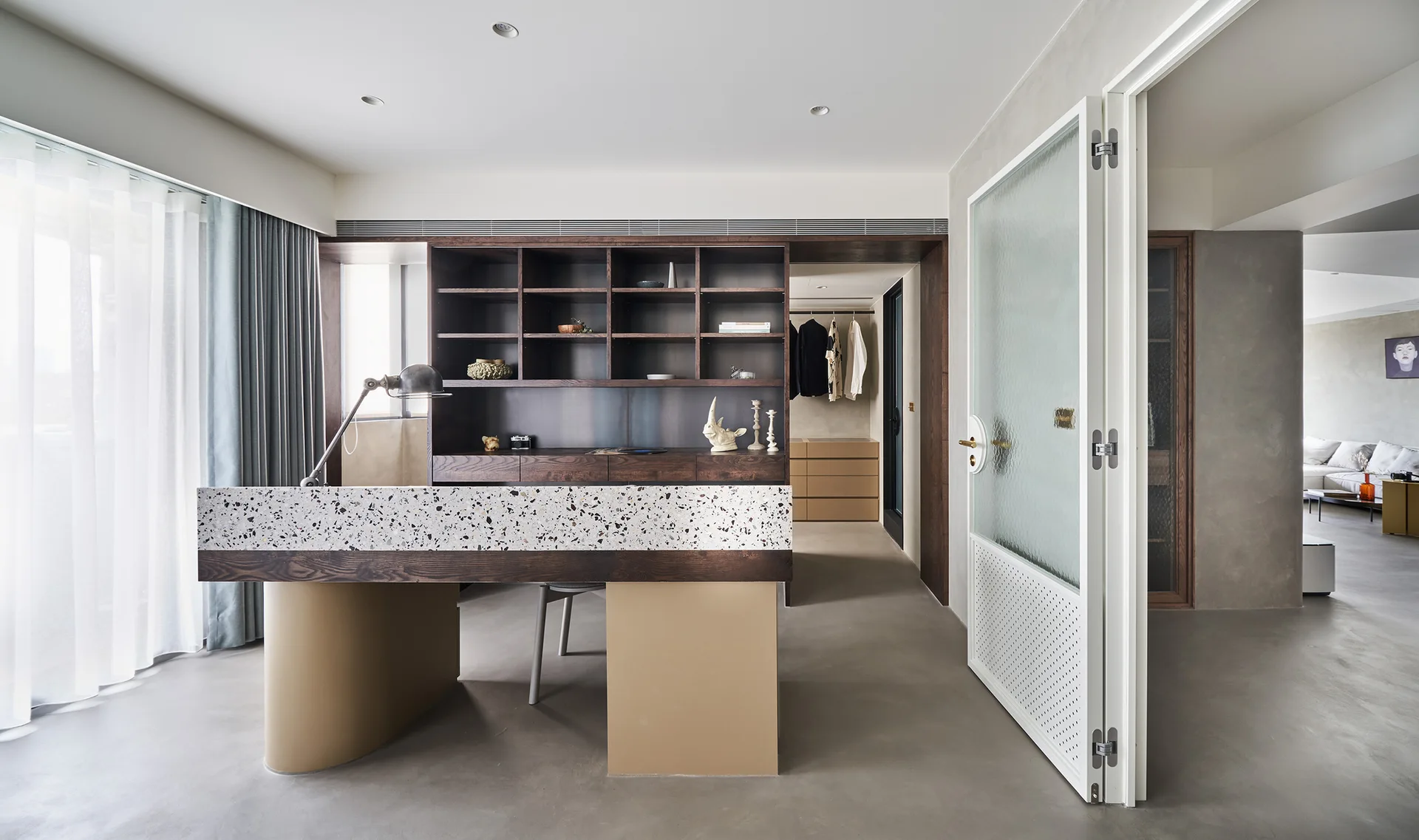A minimalist home office features a custom desk with a thick terrazzo top, a dark wood shelving unit, and smooth concrete flooring.
