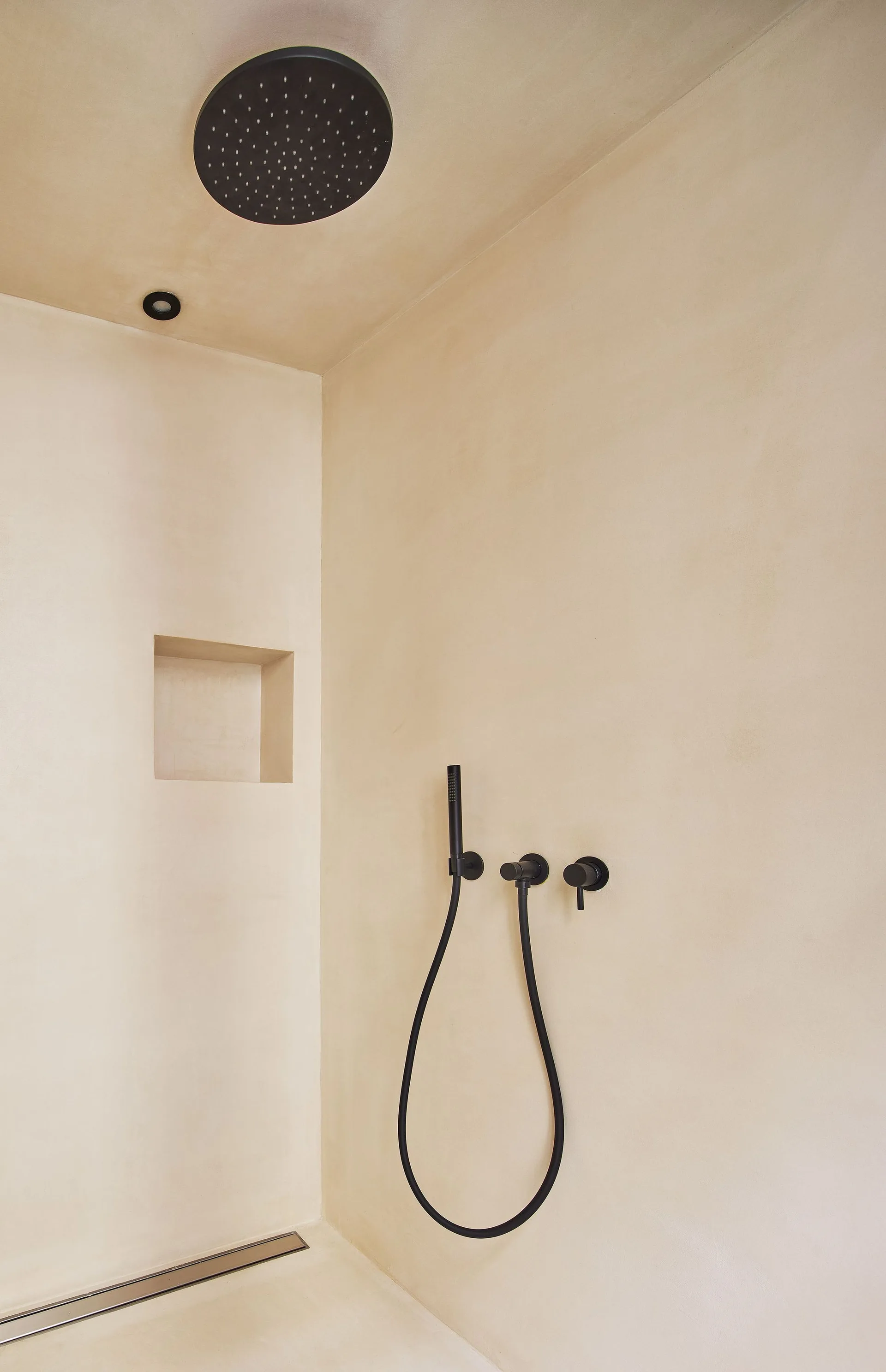 A minimalist beige plaster shower stall featuring a recessed wall niche, a linear floor drain, and matte black fixtures.