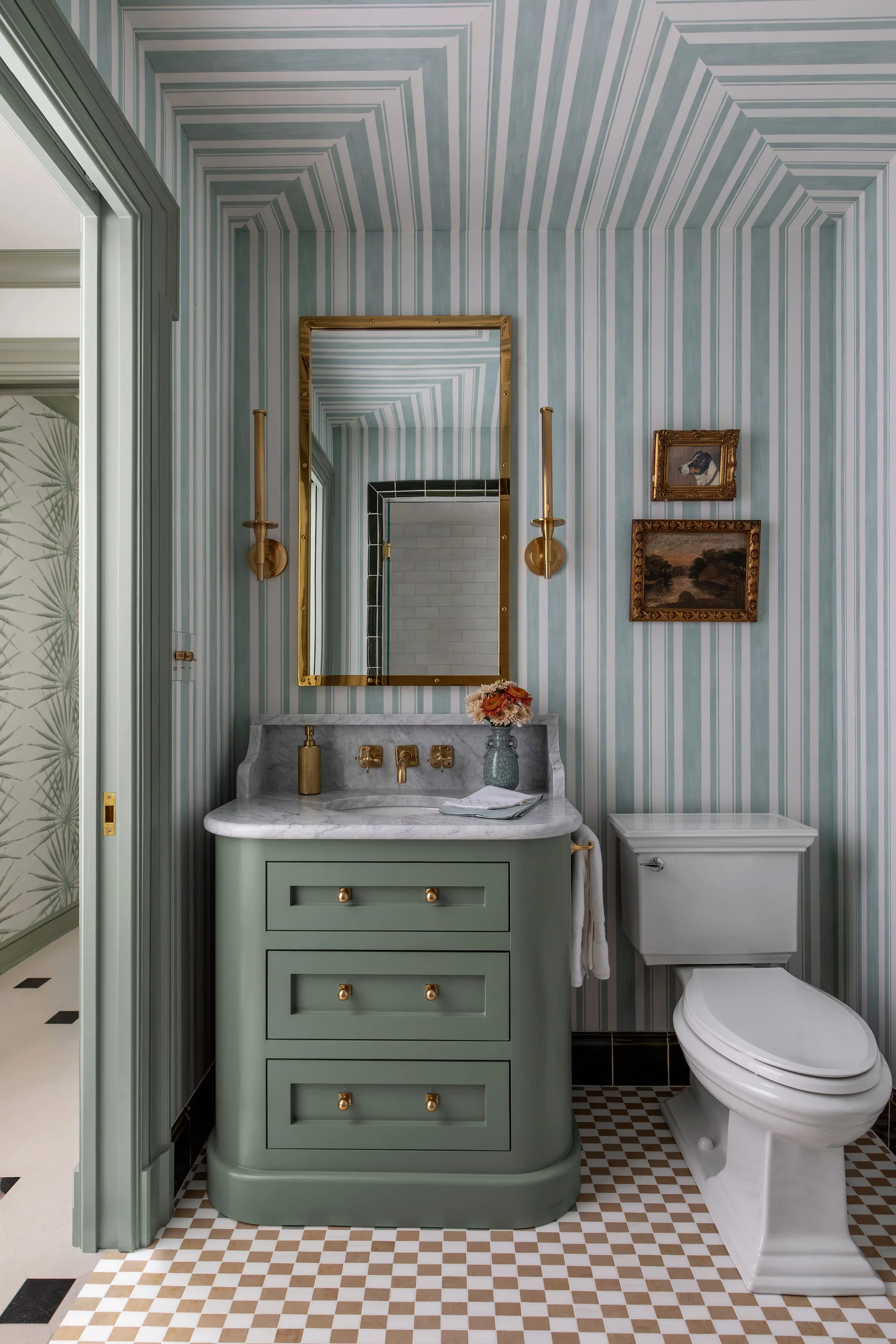A powder room features a sage green curved vanity with a marble top, blue and white striped wallpaper on the walls and ceiling, and a checkerboard floor.