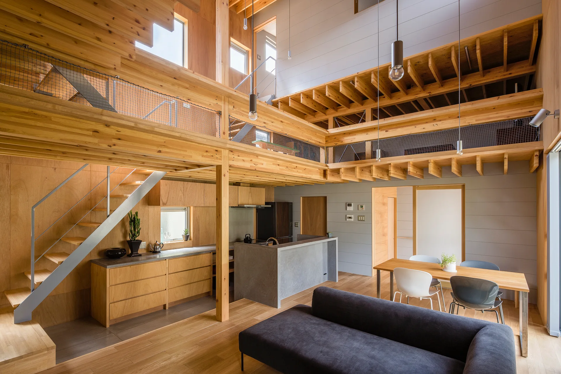 A multi-level wooden home featuring a kitchen with a concrete island, an open staircase, and a mezzanine level with netted railings.