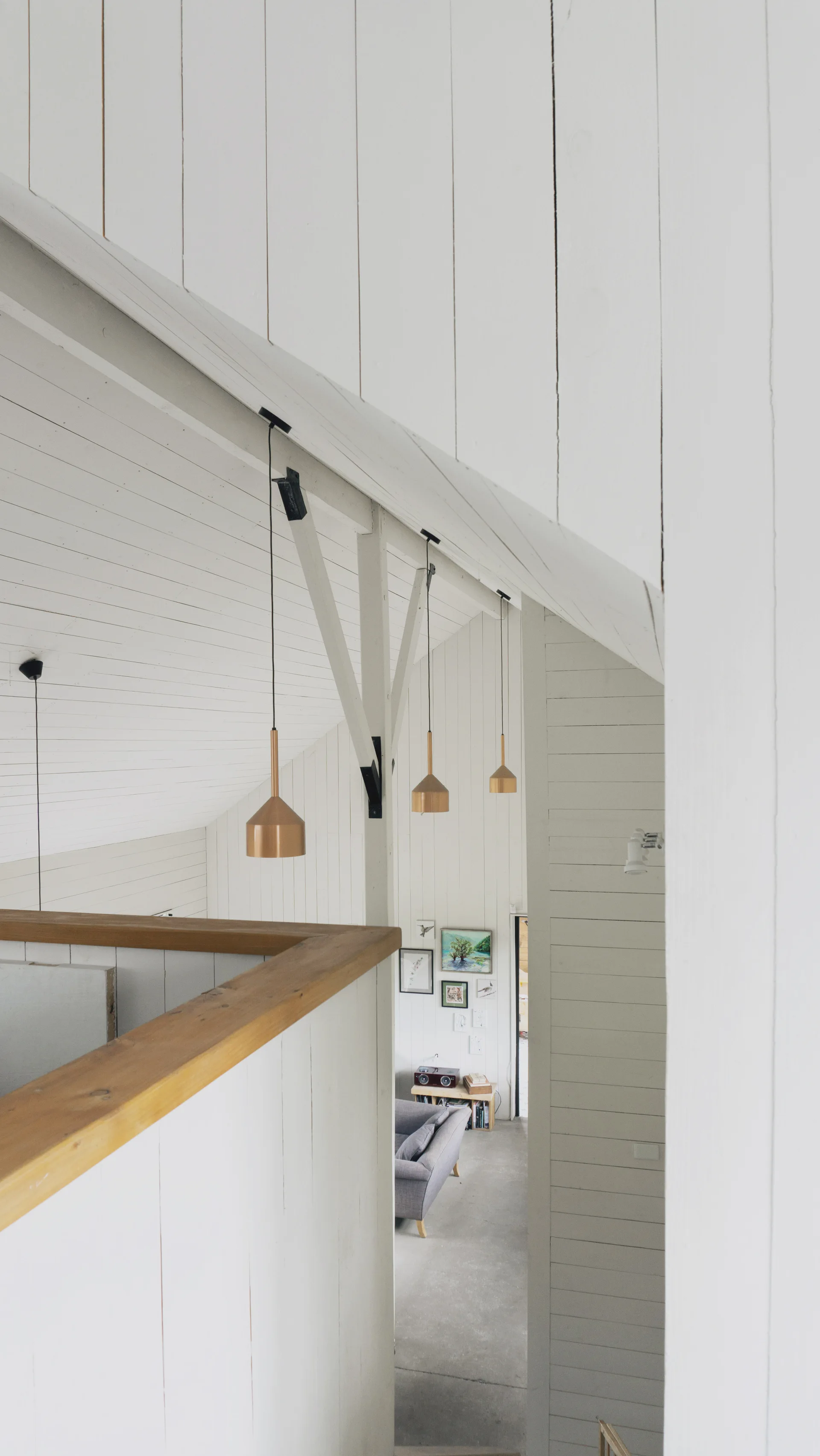 A view from a white paneled upper landing looking down into a living room beneath a vaulted ceiling with copper pendant lights.