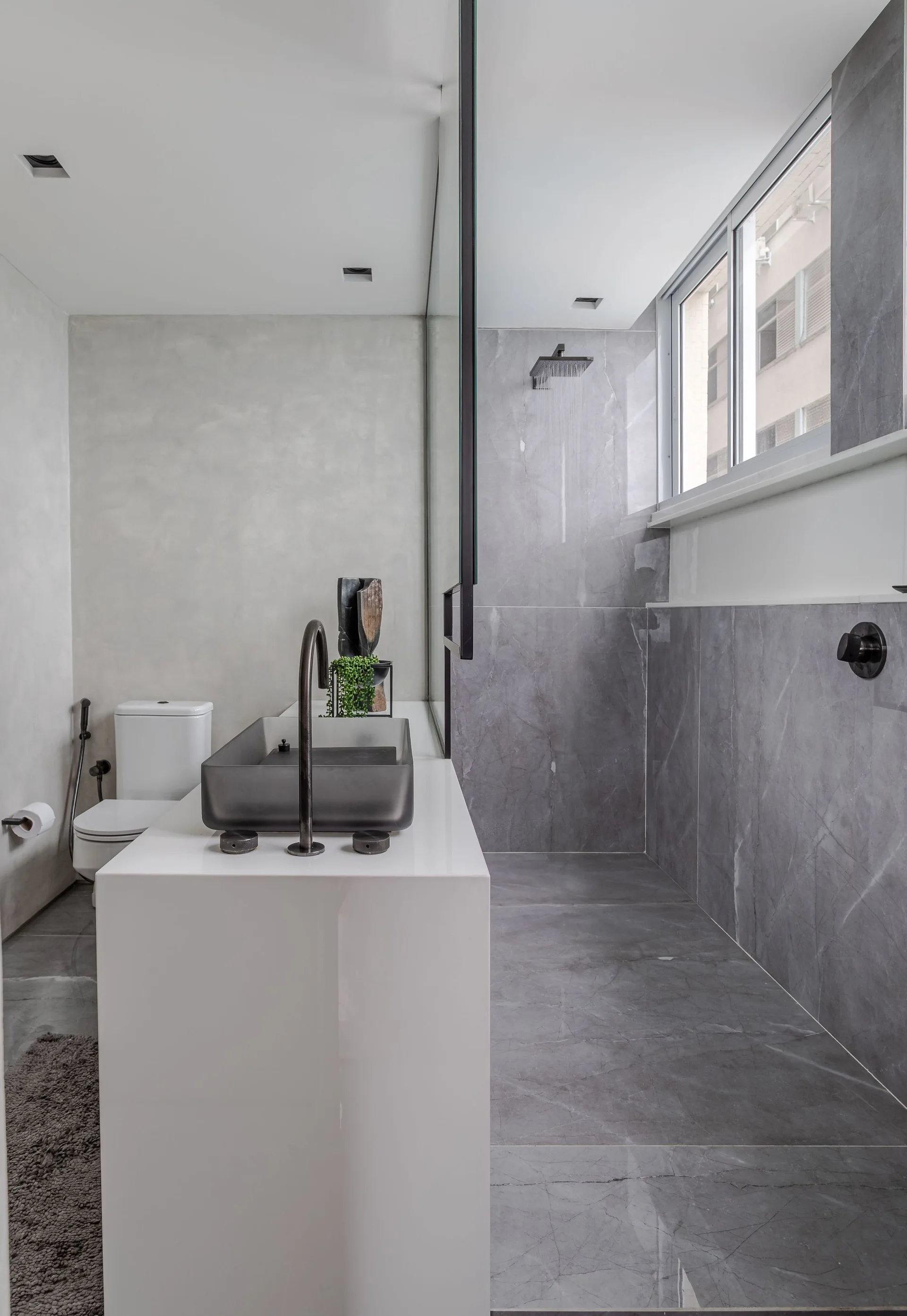 A minimalist bathroom featuring a white floating vanity with a dark vessel sink next to a shower tiled in large grey stone-look panels.