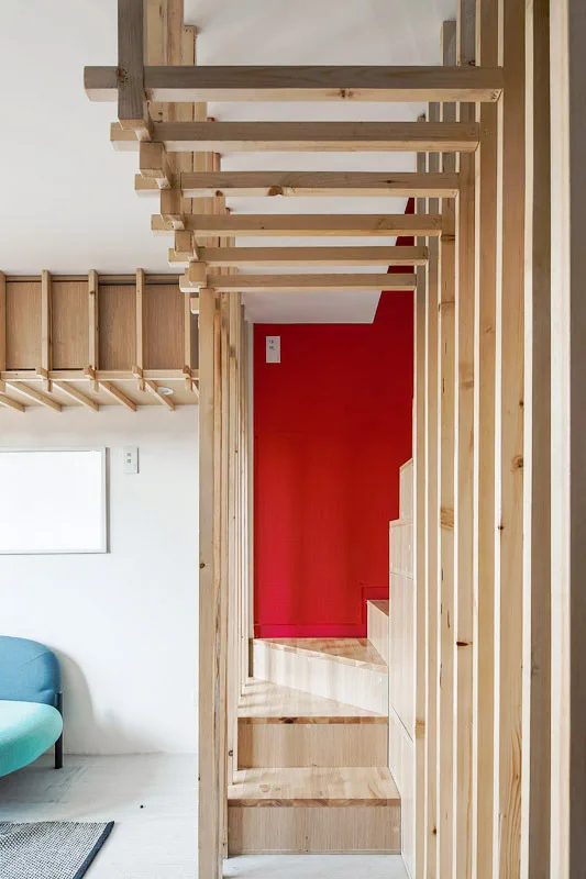 A minimalist wooden staircase enclosed by a light timber slat screen and set against a bright red feature wall.