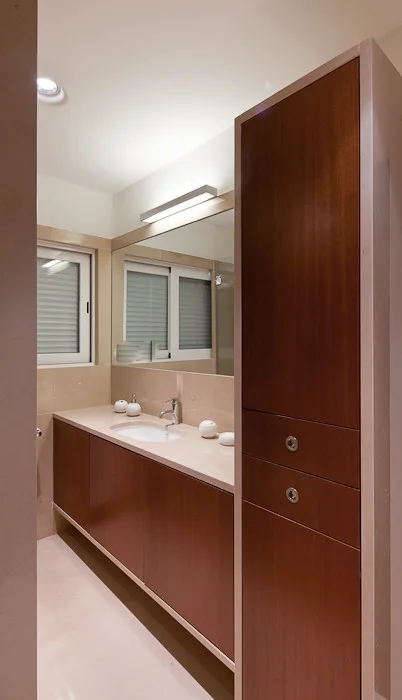 A modern bathroom features a dark wood vanity cabinet, matching tall linen tower, large mirror, and beige tiled walls and floor.