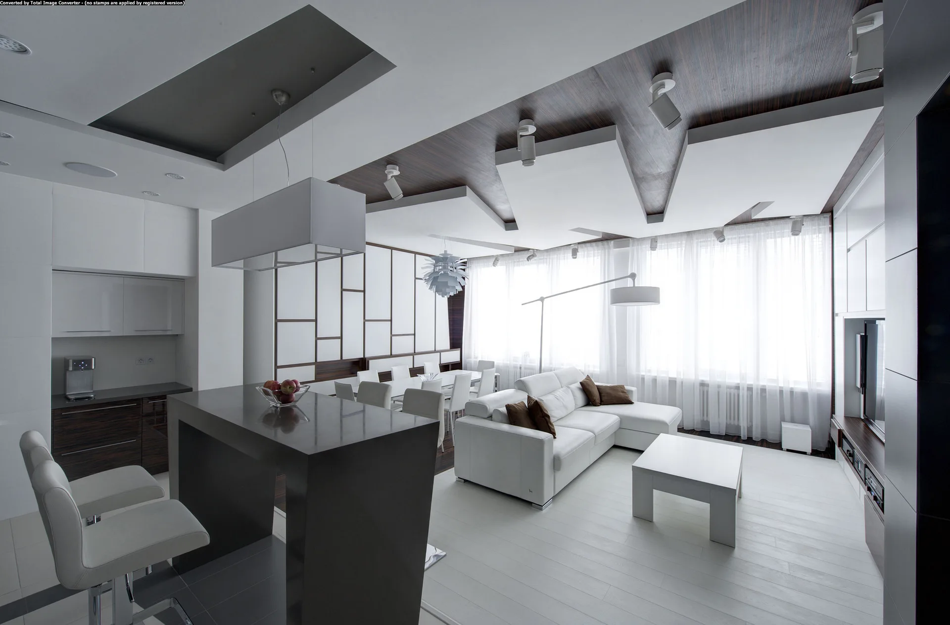 A modern open-plan living room and kitchen featuring a white sectional sofa, a dark grey island, and a geometric wood and white paneled ceiling.