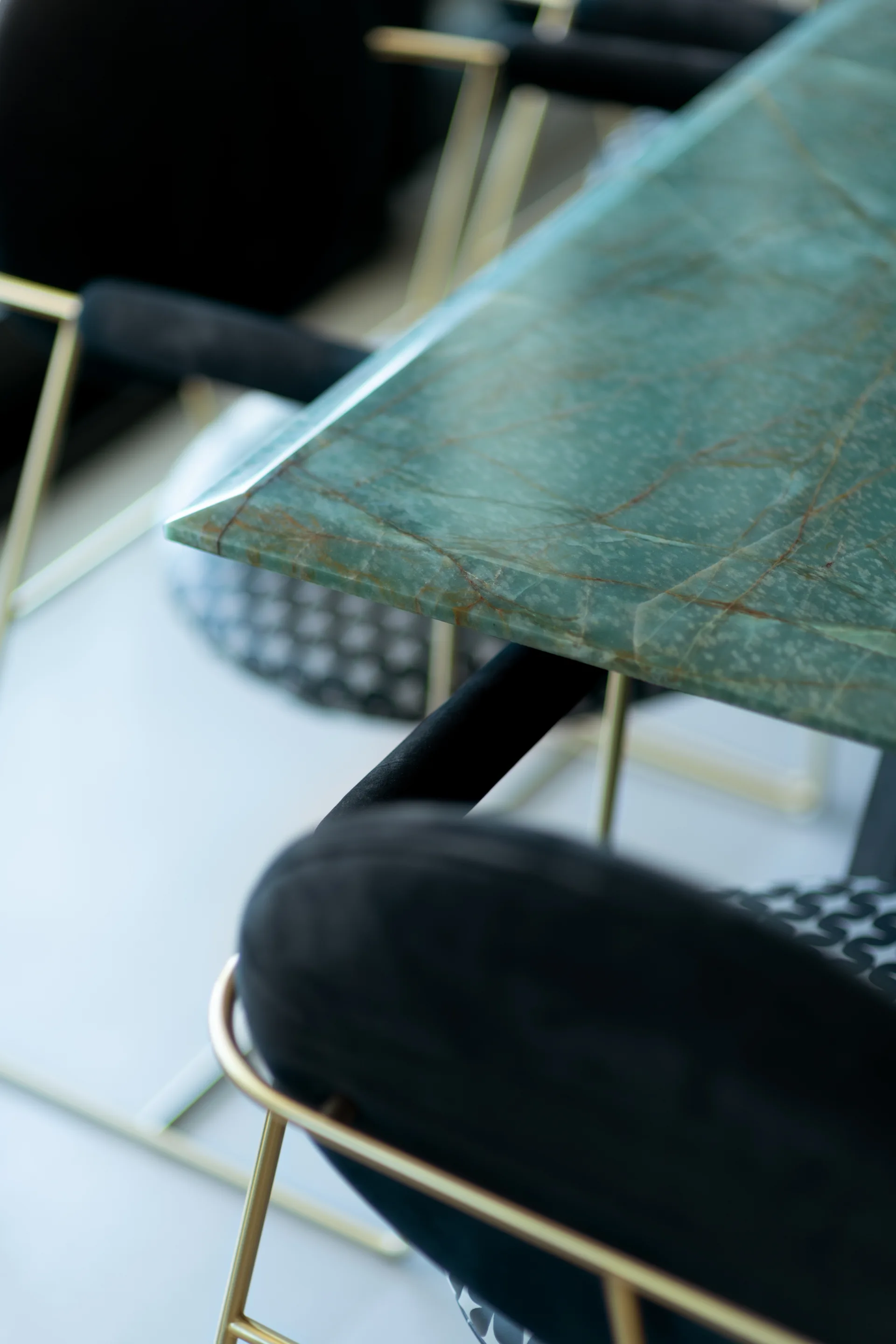A close-up view of a green veined stone dining table paired with black upholstered chairs featuring slim gold metal frames.