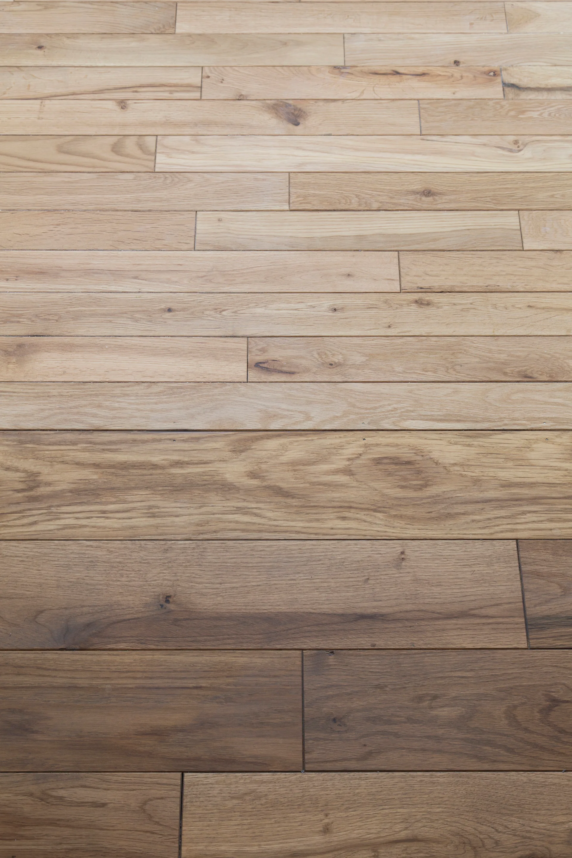 A close-up view of wood flooring planks showing a transition from light natural oak to a medium brown satin finish.