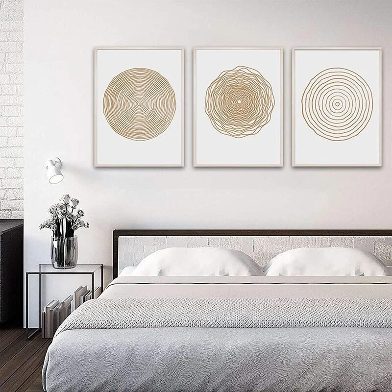 A modern minimalist bedroom featuring a bed with white linens beneath three matching framed art prints of abstract circular tree rings.