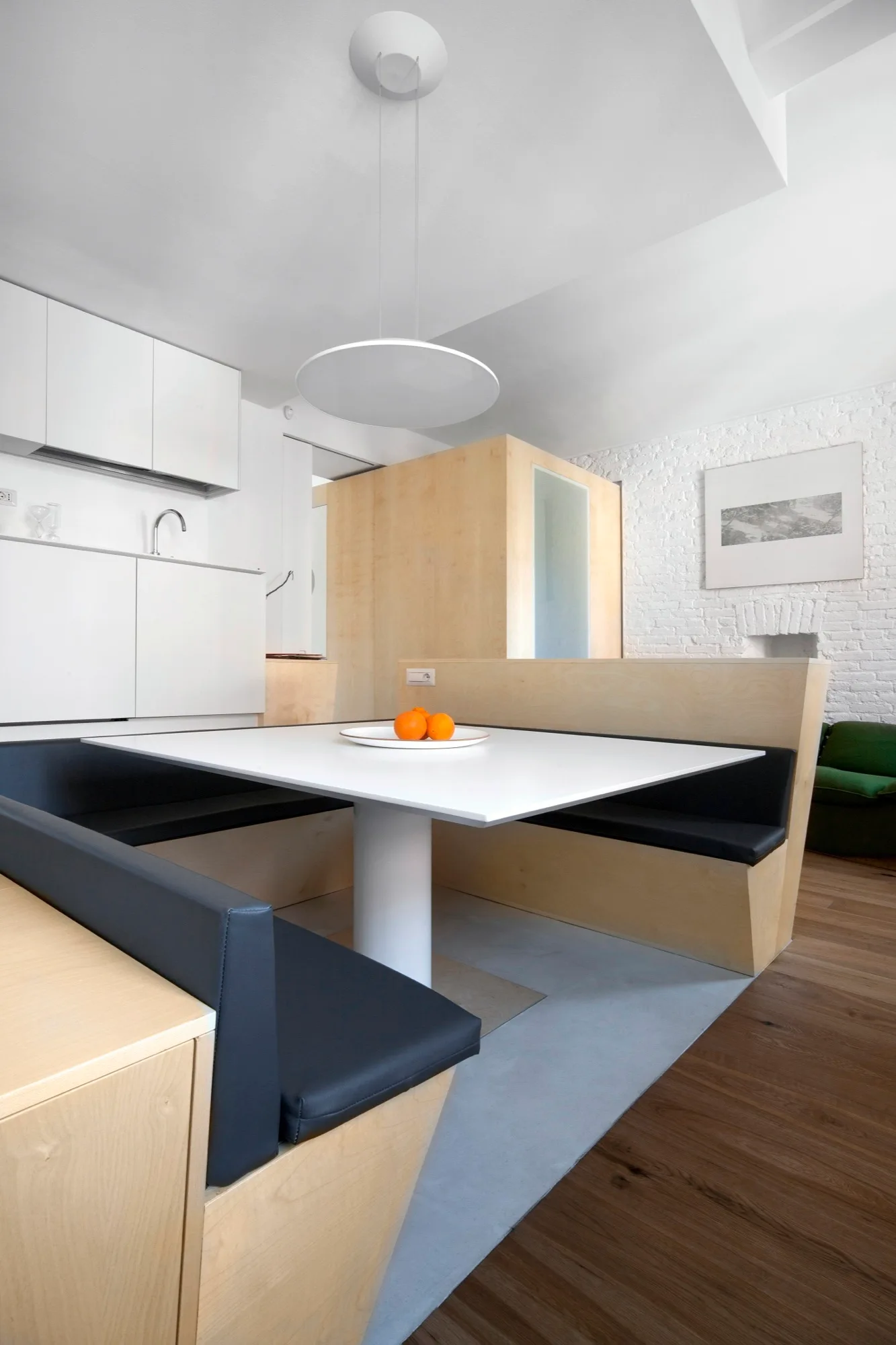 A modern dining area featuring a custom plywood banquette booth with dark cushions and a square white table.