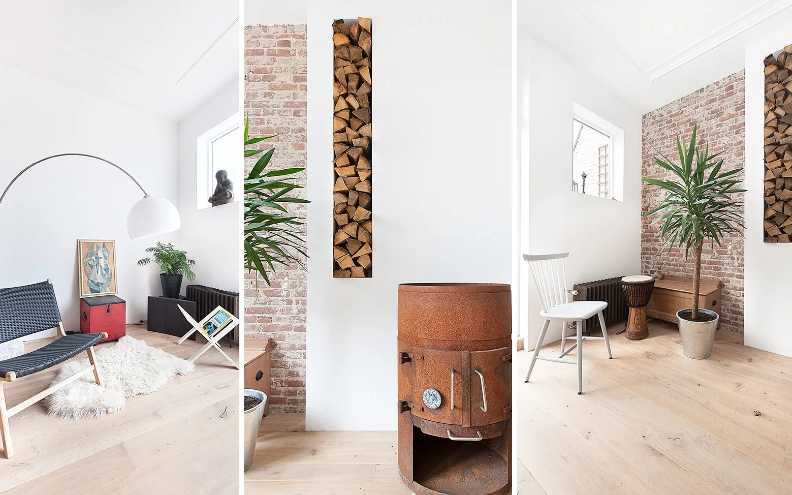 A bright living room features a rusted metal cylindrical stove, a vertical wood log storage niche, an exposed brick wall, and a woven lounge chair.