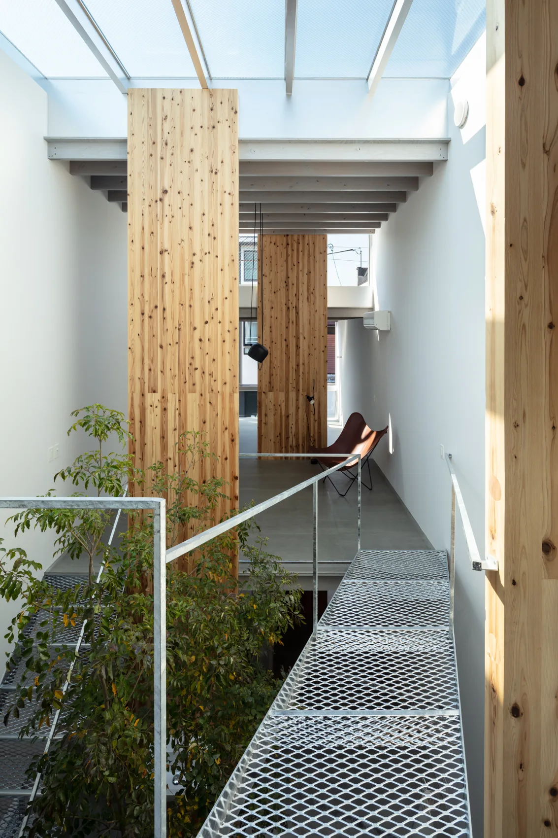 A modern minimalist interior featuring a galvanized metal mesh bridge, vertical wood-plank accent walls, and a glass skylight roof.